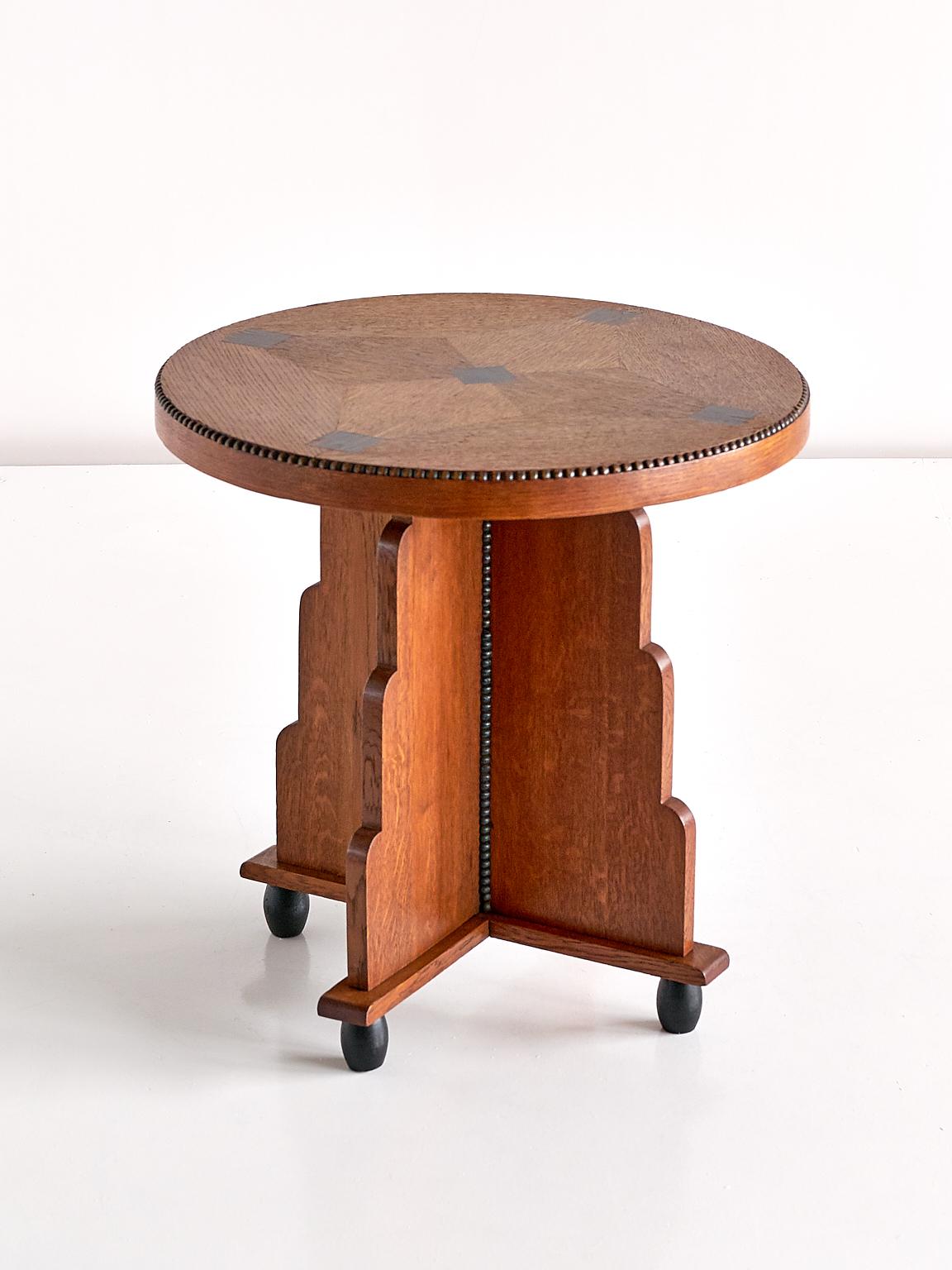 This elegant Art Deco side table was produced in The Netherlands in the early 1930s. The tiered base in solid oak stands on four rounded feet in dark stained oak. The striking round top is inlaid with a geometric pattern in veneered oak and veneered