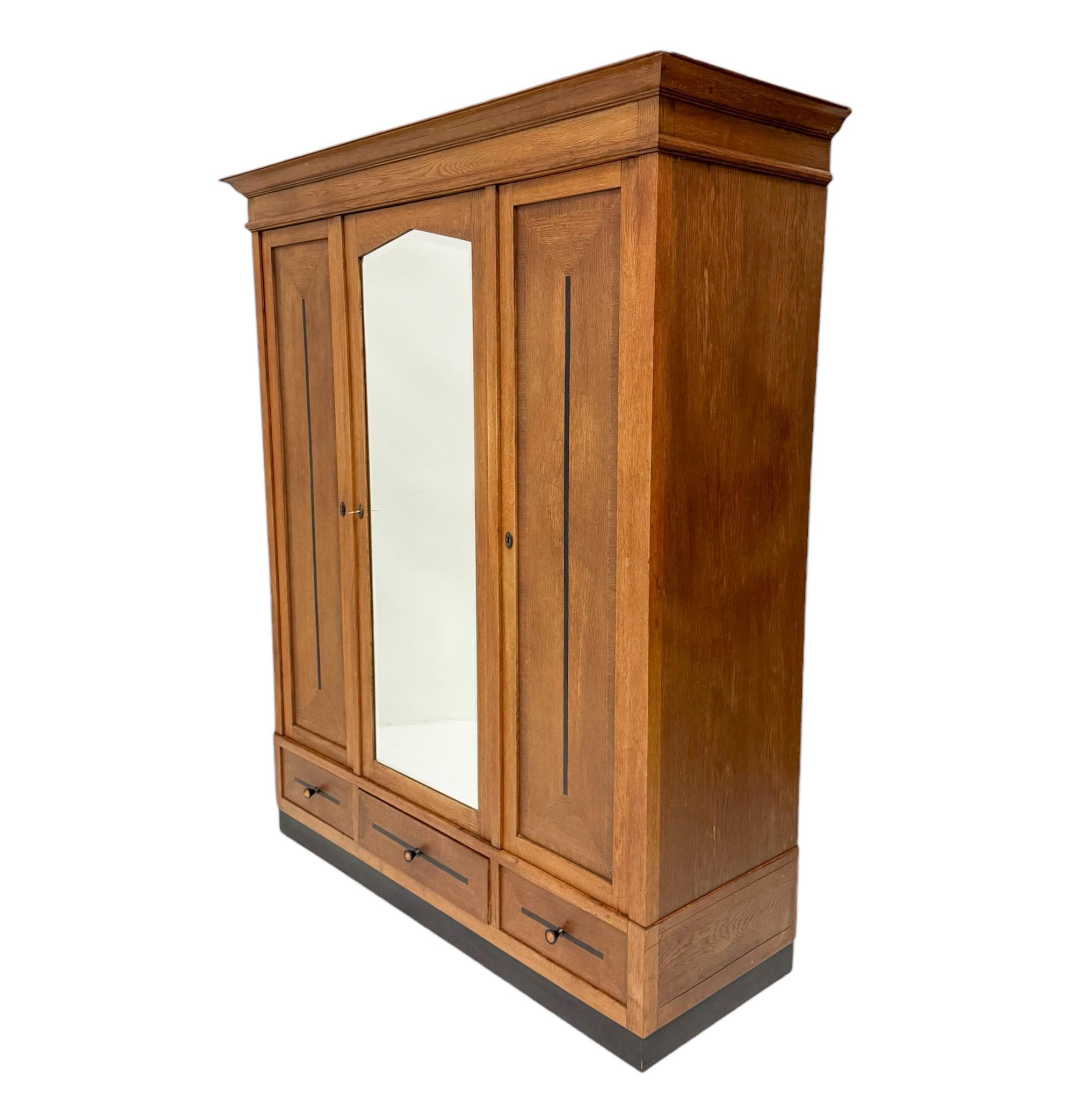 Stunning and elegant Art Deco Amsterdamse School three-door armoire or wardrobe.
Striking Dutch design from the 1920s.
Solid oak and original oak veneer base with original beveled mirror in the middle door.
Behind the right door and left door there
