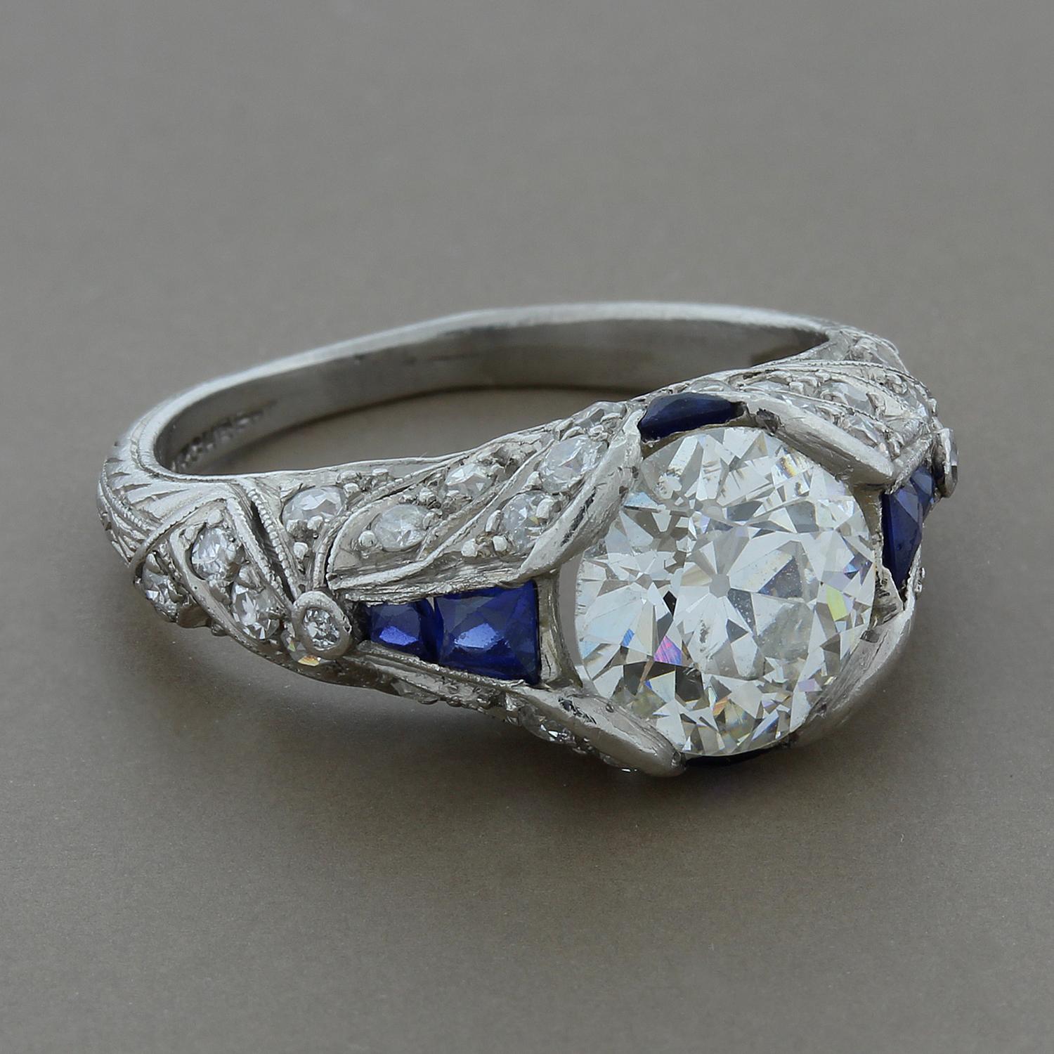 A spectacular art deco ring featuring a brilliant 2.20 carat round antique cut diamond at the center. The feminine platinum setting is complemented by 0.70 carats of diamonds and blue sapphires in a design reminiscent of the era. 

Currently ring