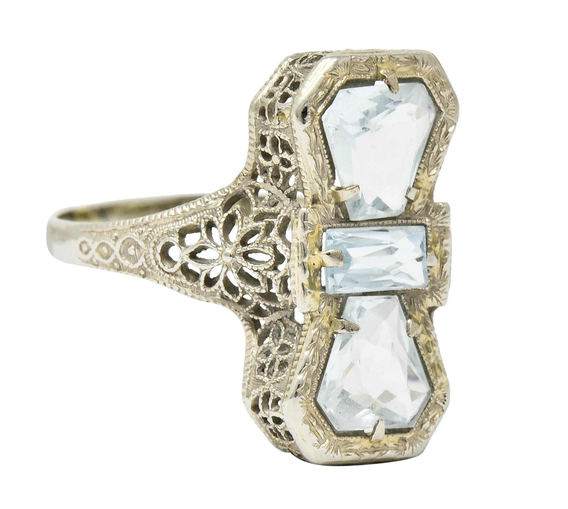 Hour glass shaped dinner ring features three fancily cut aquamarines

Very well-matched in very light greenish-blue color

Mounting is intricately pierced with floral motifs and accented by milgrain

Stamped 14K for 14 karat gold

Circa: 1930s

Ring