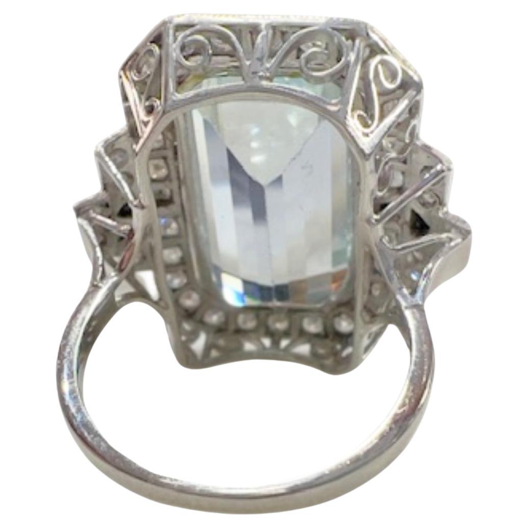 This Art Deco-style ring is crafted in Platinum 950 and features an aquamarine and diamonds. It has a weight of 11.2 grams and is sized ES 13.5 / EU 53.5 / US 6.5 / 17 mm. The ring is adorned with a central emerald-cut aquamarine, weighing 11.90