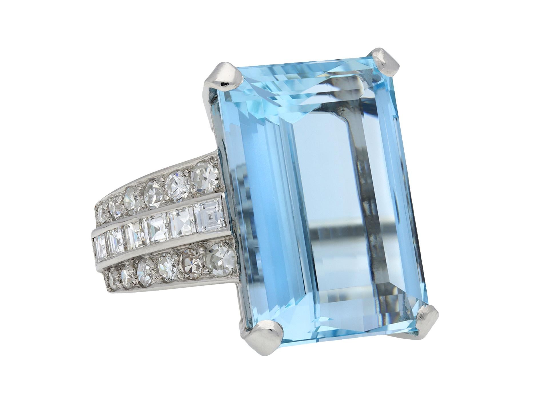 Art Deco aquamarine and diamond ring. Set to centre with a rectangular emerald-cut natural aquamarine in an open back claw setting with an approximate weight of 16.66 carats, flanked either side by two rows of round eight cut diamonds in open back