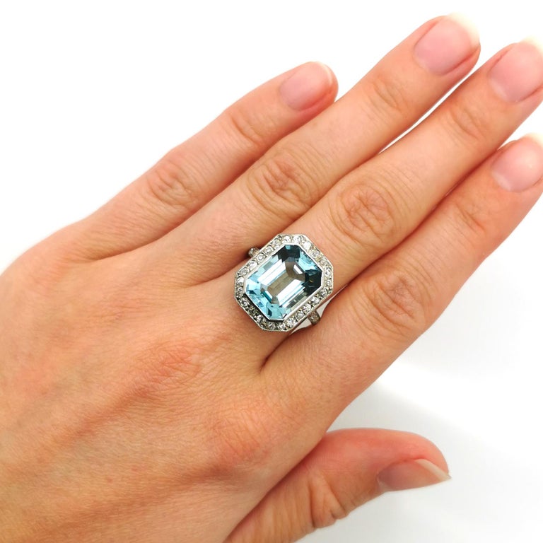 An aquamarine and diamond ring, set with an emerald-cut aquamarine, in an Art Deco mount, with a central rub over setting, and an eight-cut diamond set pavé surround, with millegrain edges, mounted in platinum. The estimated weight of the aquamarine