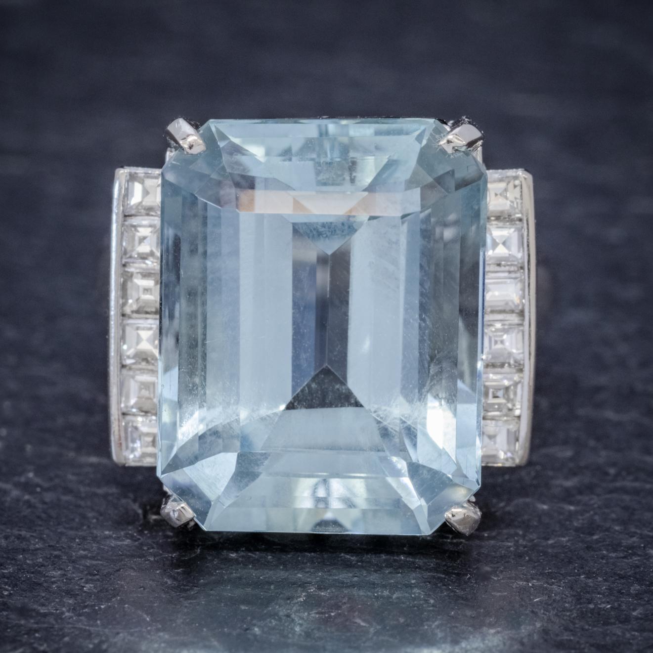 A magnificent Art Deco cocktail ring set with a breath-taking emerald cut Aquamarine which is a lovely clear ocean blue colour weighing approx. 12ct and flanked with a row of six square cut Diamonds down each side. 

The Diamonds are clean, bright