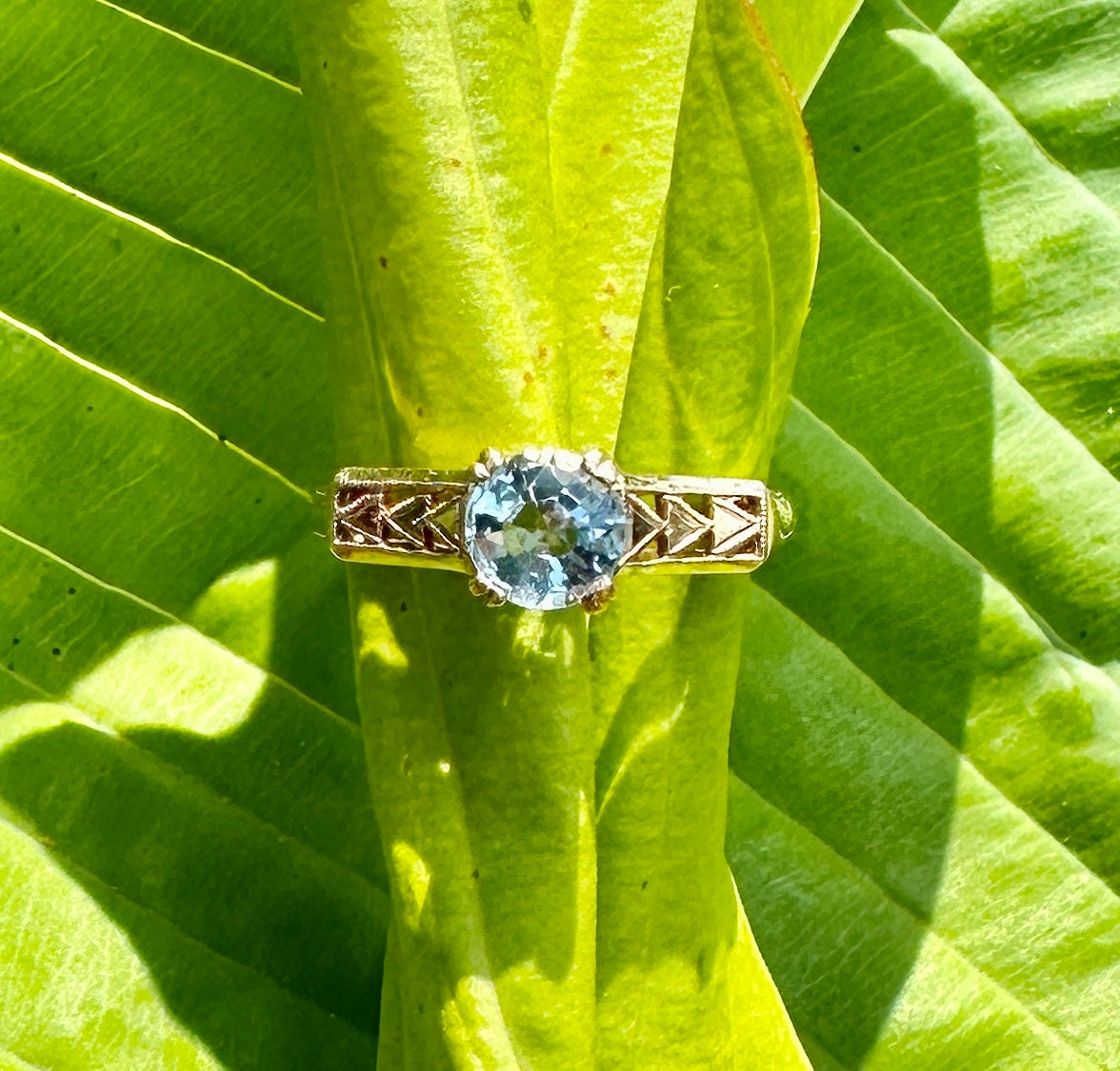 This is a stunning Art Deco 1 Carat Round Brilliant Cut Aquamarine Solitaire Wedding Engagement Stacking Ring in a 10 Karat Yellow Gold ornate open work setting of great beauty.  The ring has a gorgeous Aquamarine gem with lovely Aquamarine blue