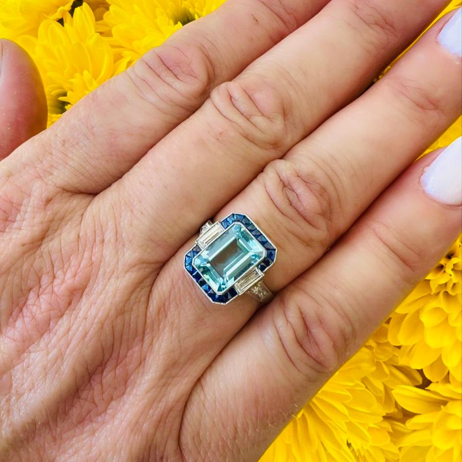 This is a lovely example of Art Deco elegance! The platinum ring features a sky blue rectangular-cut aquamarine measuring approximately 10.0 x 7.0  x 4.7mm and weighing 2.36 carats, flanked by two straight baguette-cut diamonds, framed by Swiss-cut