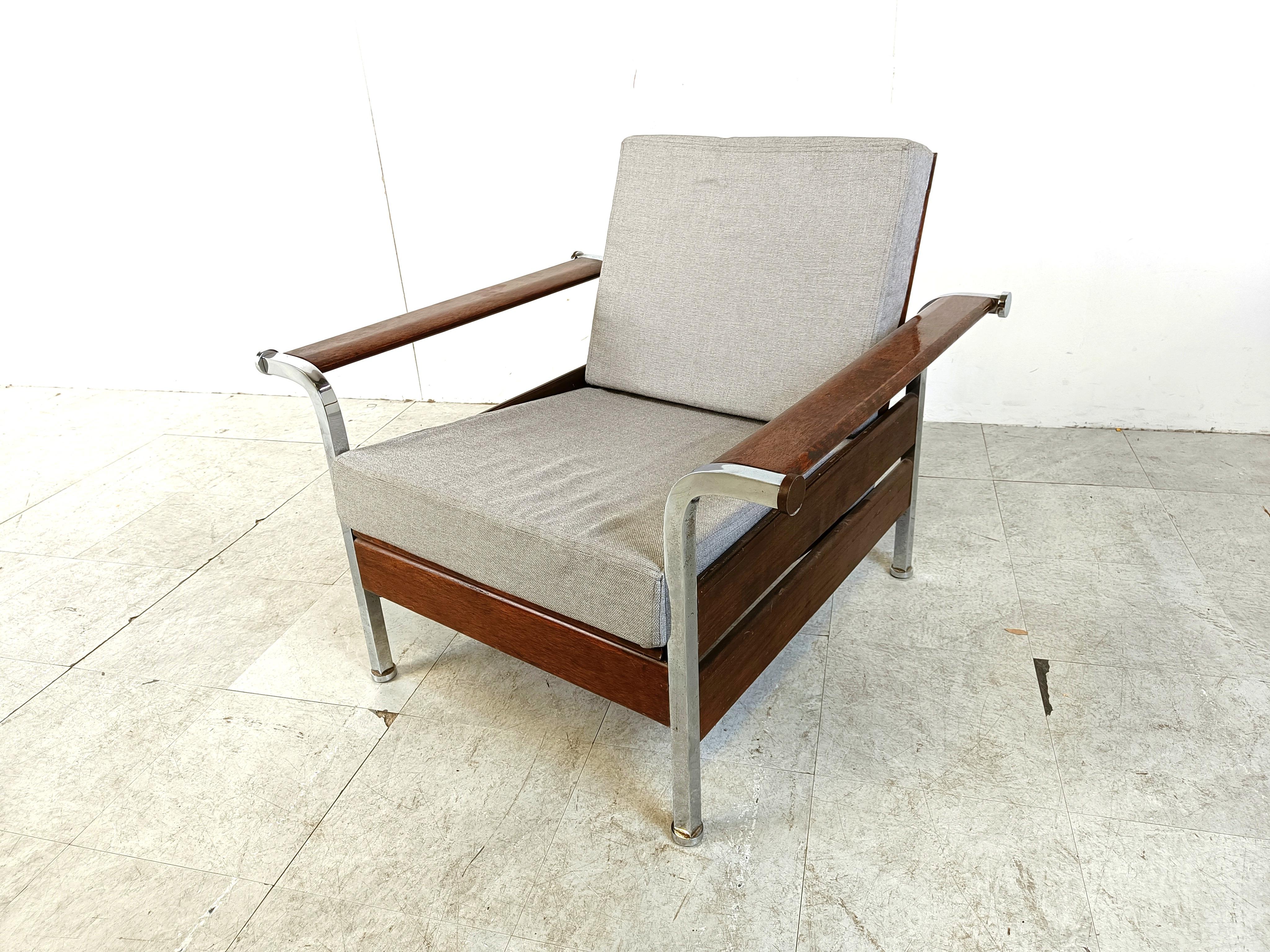 Sillón de inspiración art déco con armazón de madera y cromo y cojines de tela gris.

La silla data de los años 50, cuando muchos diseños aún estaban muy inspirados en el art déco.

Bonitas patas de metal cromado y un robusto armazón de