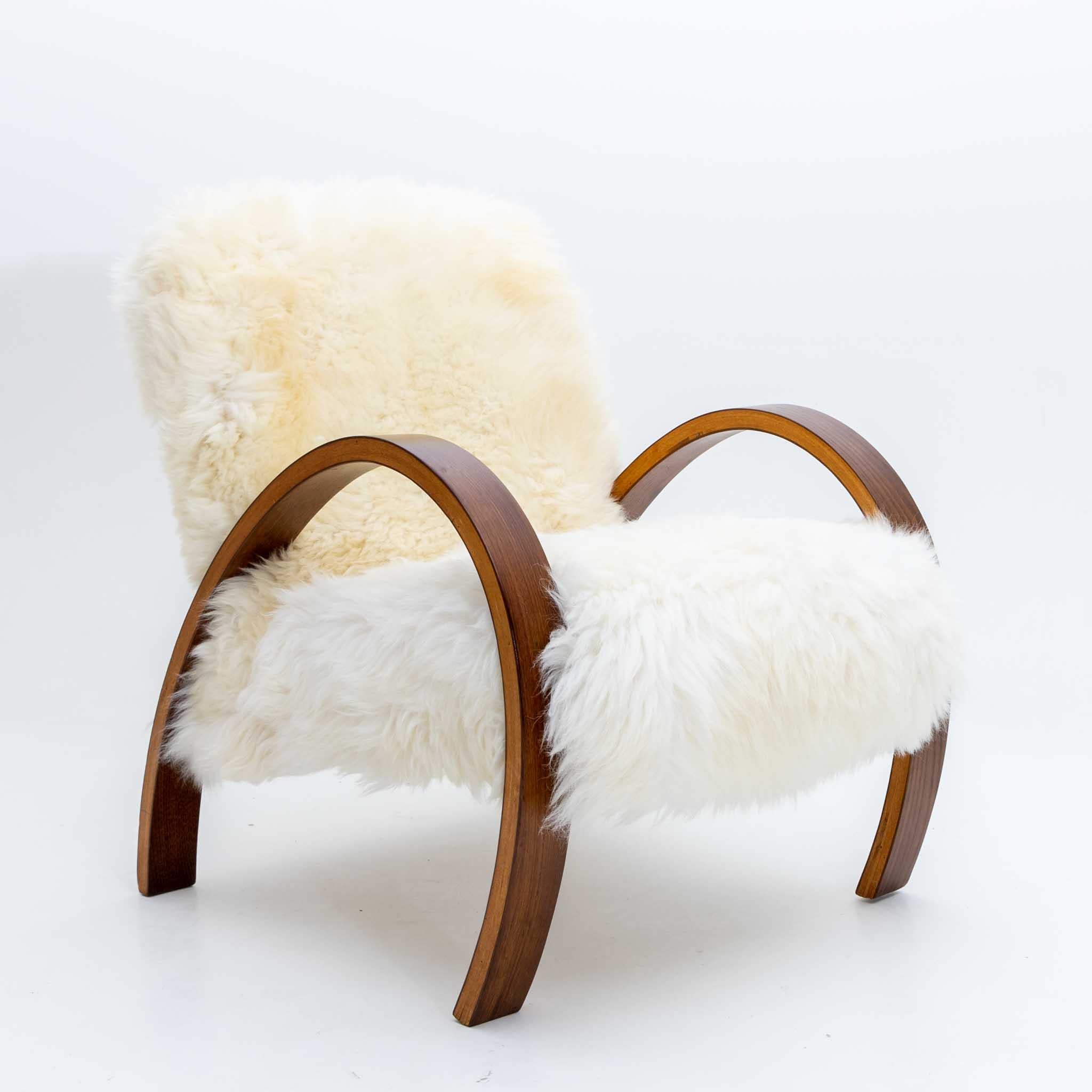 Armchair with elegantly curved armrests made of plywood with dark stained tops. The armchair has been newly upholstered with a genuine sheepskin.