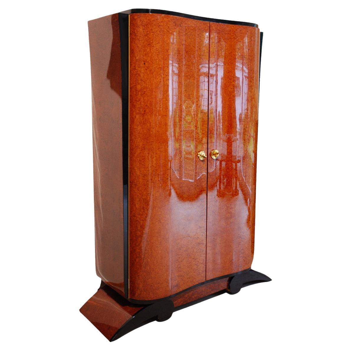 French Art Deco period Armoire circa 1930s.

Curved front doors with wonderful Amboina Burl veneer. Restored with piano lacquer high-gloss finish.
Some parts are lacquered in black, the sides are also veneered with amboina burl.

Original brass