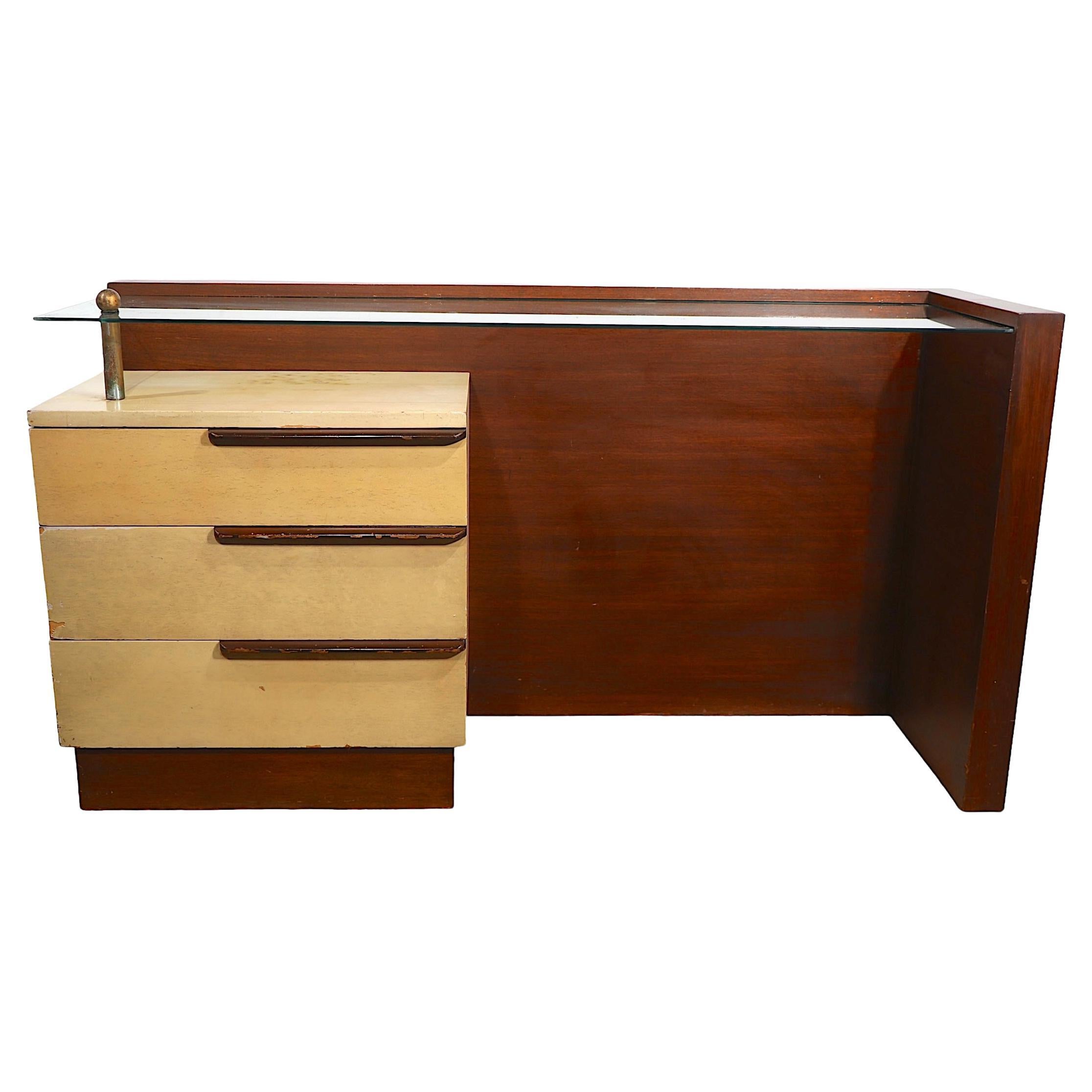 Iconic Art Deco, Art Moderne vanity designed by Gilbert Rohde for Herman Miller, circa 1936. The vanity features a bank of three drawers, which supports a floating glass top surface, that extends the width of the vanity and is framed by  a walnut