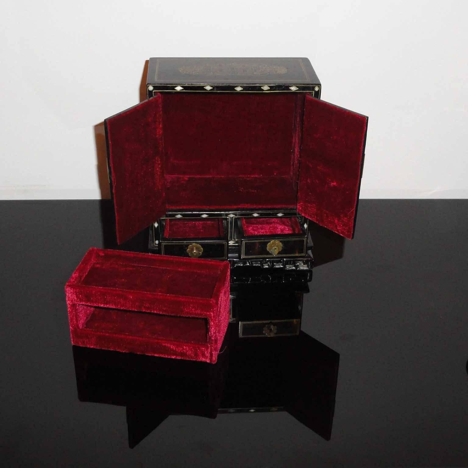 Art Deco Asian decor jewelry box with mother of pearl inlay.
Jewelry box, black lacquered wood, shaped as a small two-door cabinet with two drawers, inside with vivid red peluche (velvet). Doors decorated with mother of pearl inlays, gold painted