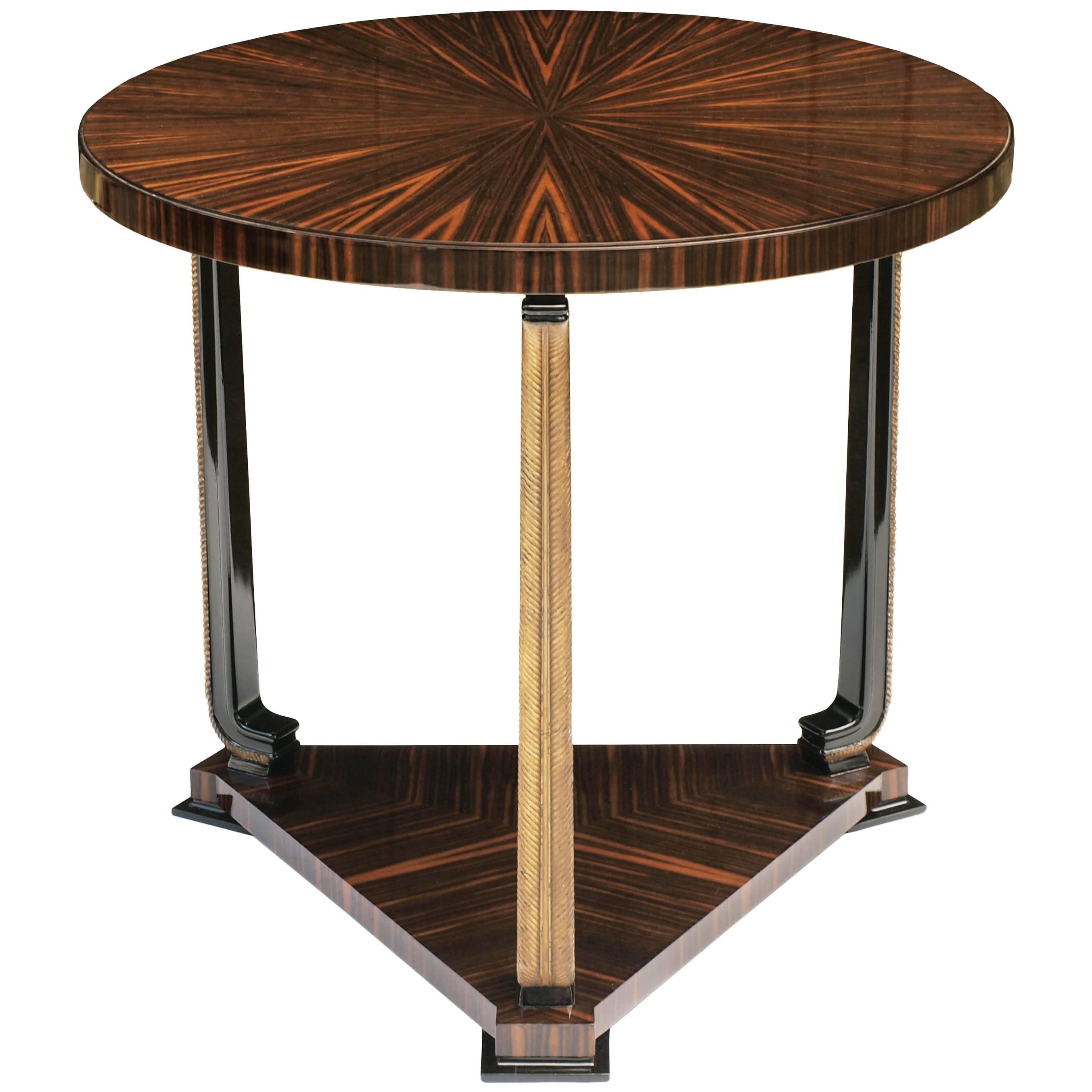 An exceptional ebony Macassar and parcel-gilt circular table by Axel Einar Hjorth for Nordiska Kompaniet, circa 1928.

The sunburst top is of matched ebony Macassar with a stepped fashion edge, supported by three carved parcel-gilt palm shaped legs