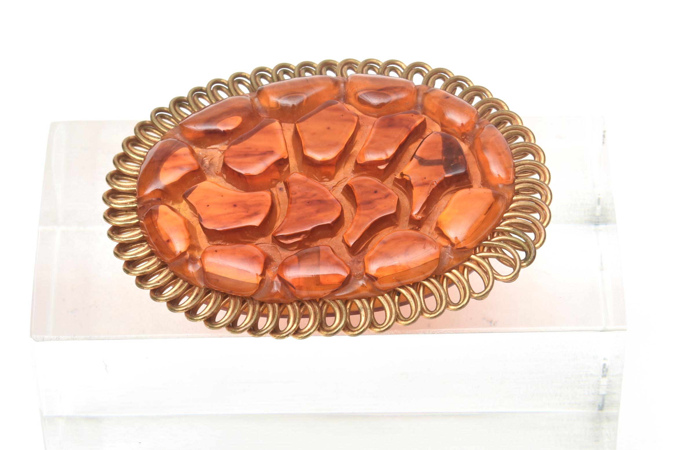 This fabulous carved art deco bakelite and brass trimmed oval pin brooch will make any outfit sing. The brass is overlapping loops as the exterior.
This is not a common bakelite pin. The color of the bakelite has beautiful tones of orange amber