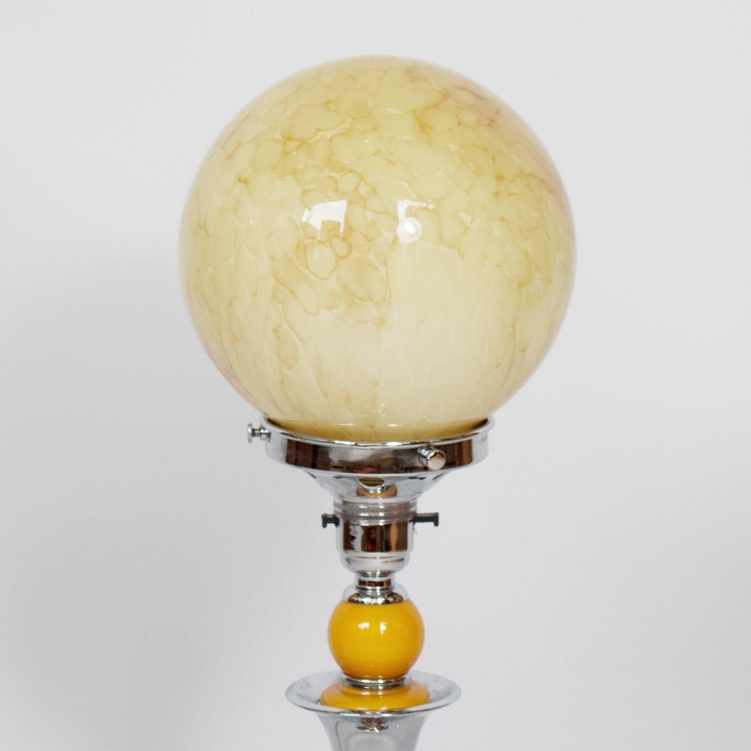 A chromed metal and bakelite table lamp. Marbled yellow glass globe, over a chromed metal stem with yellow bakelite ball to top and bottom of stem. Circular chromed metal base. 

Dimensions: H 47cm, D of shade 14cm, D of base 13cm

Origin: