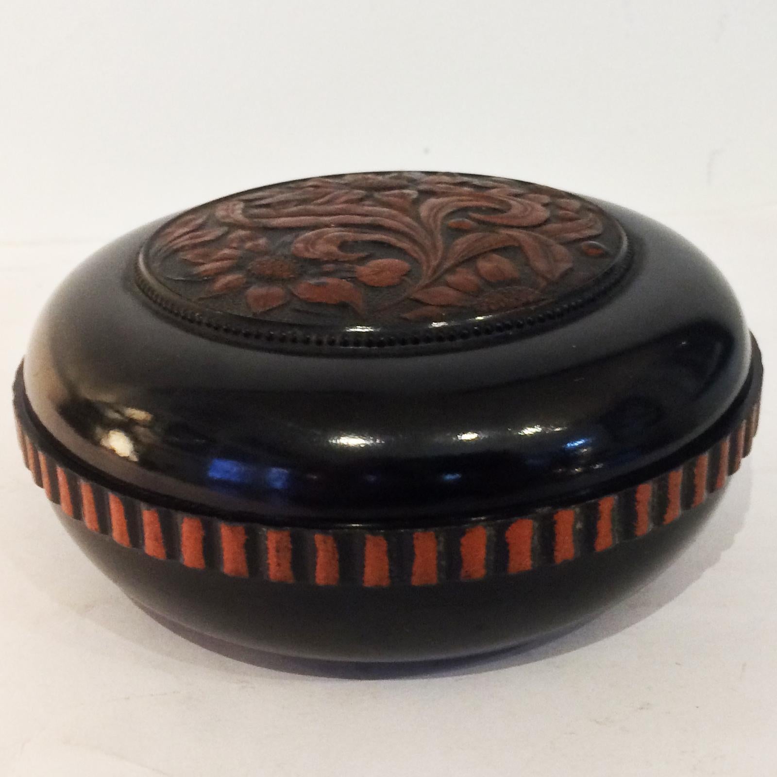 Art Deco carved bakelite and painted gilt highlights, storage box. Very dark brown to black with the bronze highlights to the daisies and leaves to the relief on the screw top cover and coin edge recesses to the lower bowl. The Bakelite is all in
