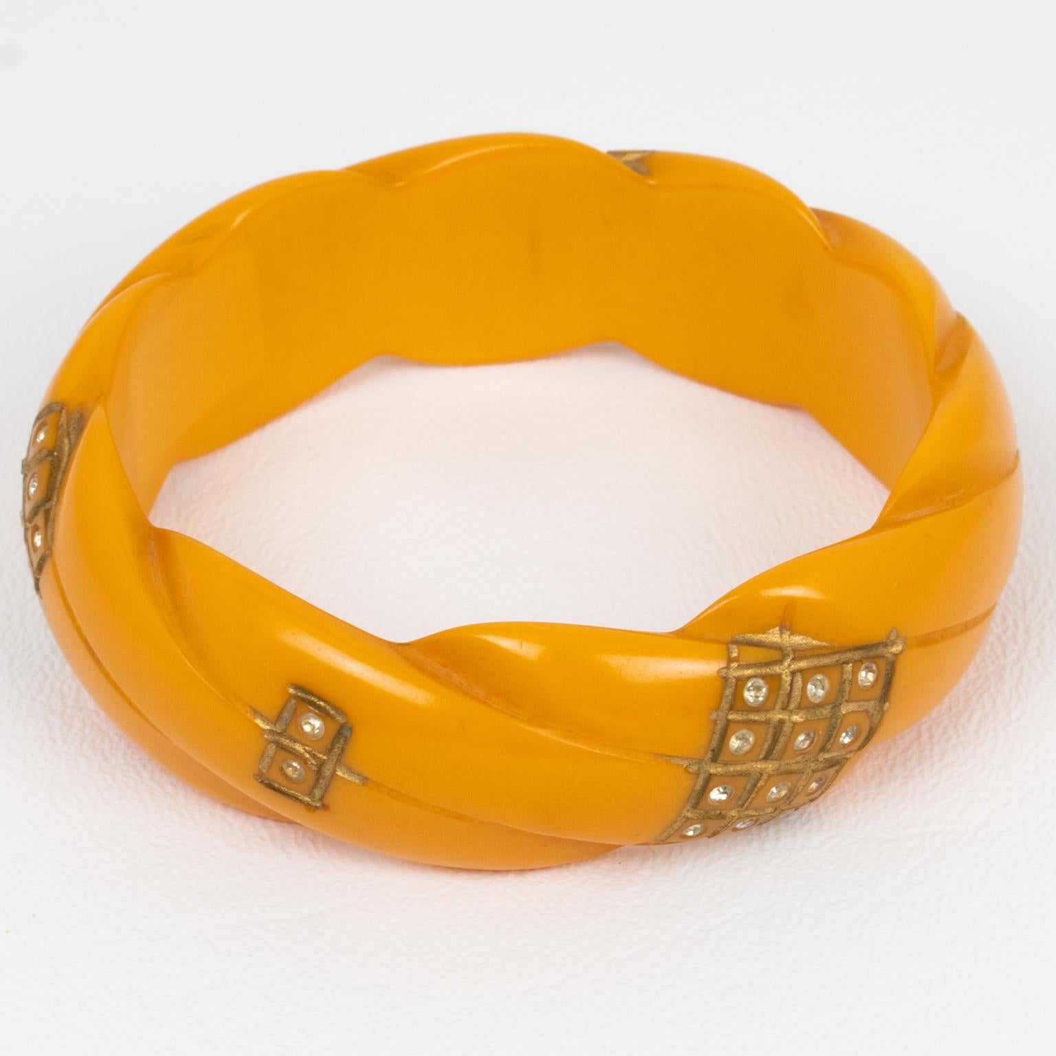 This elegant Art Deco Bakelite bracelet bangle was crafted in France in the 1930s. The piece features a chunky domed shape with braided geometric carving all around it and is ornate with gilded paint application and tiny clear crystal rhinestones.