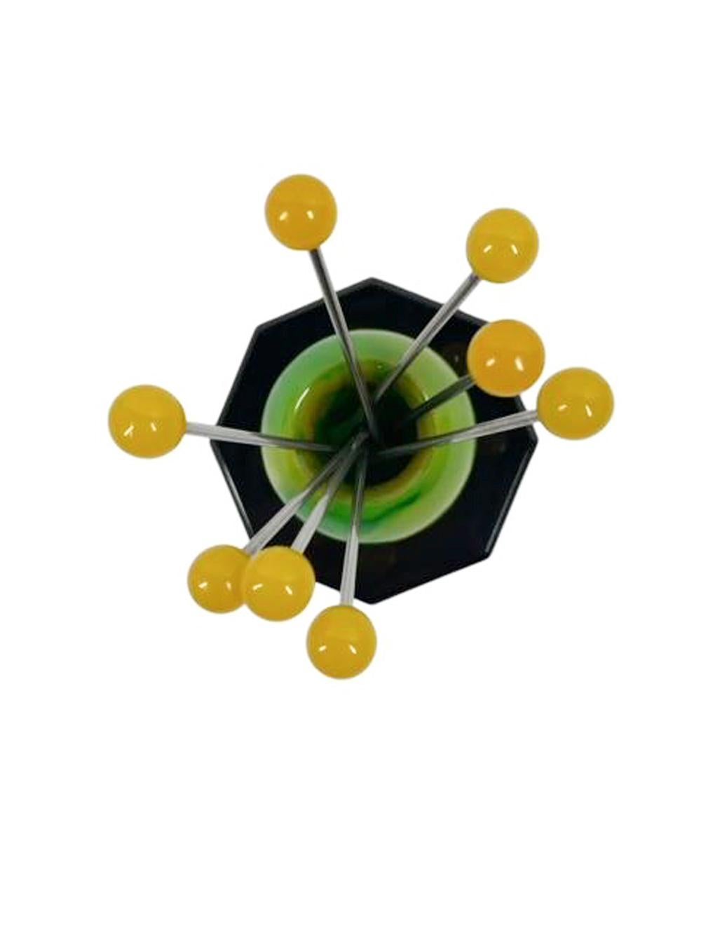 Set de pics à cocktail Art Déco en bakélite - huit pics fourchus avec des boules jaunes dans une sphère tourbillonnante verte et jaune sur une base octogonale noire.