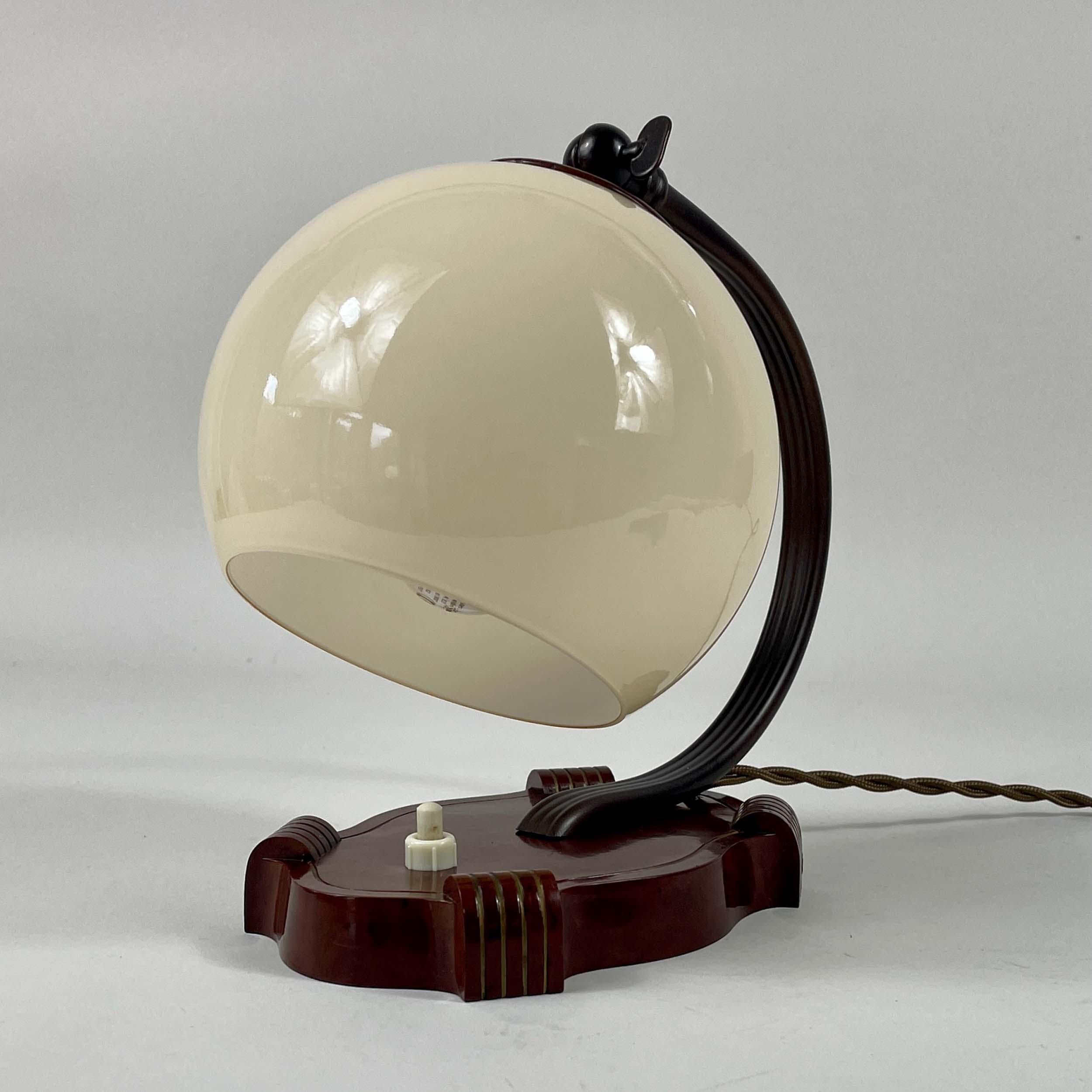 Cette lampe de table ou de chevet Art Deco a été conçue et fabriquée en Allemagne dans les années 1930, pendant la période du Bauhaus.

La lampe présente une base sculpturale en bakélite dans un riche ton brun rougeâtre / châtaigne avec des détails