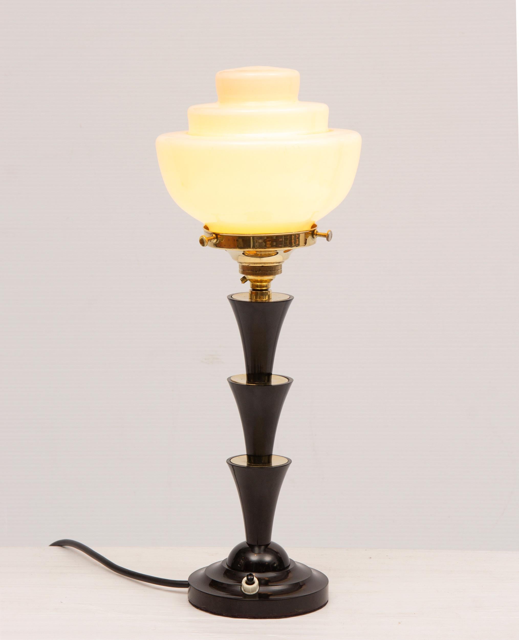 Art Deco triple cone Bakelite table lamp with original stepped pink glass shade.
Black and brass stem contoured in the manner of a palm tree
Measures: H 41 cm, W 17 cm, D 17 cm.
British, circa 1930.
 