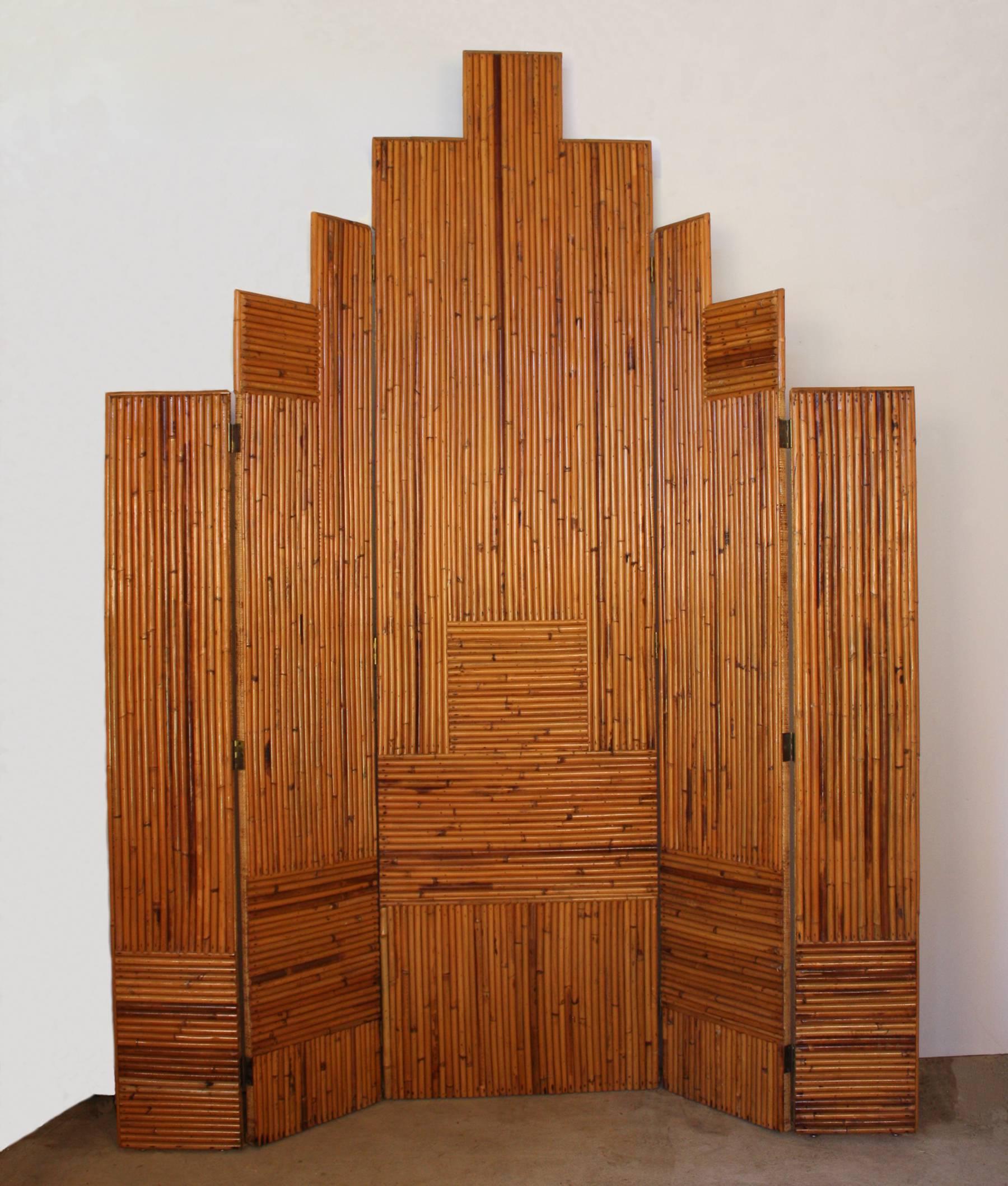 An Art Deco five-panel screen or room divider with split bamboo reeds on one side and woven natural fiber on the reverse side. The screen is constructed of sturdy 3/4-inch wood panels that, together, resemble a city skyline. circa 1960.