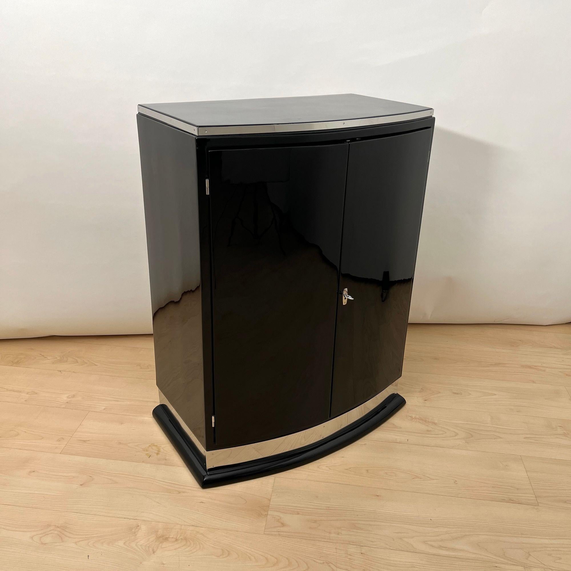 Eleganter, kleiner Art Deco Barschrank mit 2 Türen aus Frankreich um 1930.

Hochglänzender schwarzer Klavierlack auf nussbaumfurniertem Korpus. Zierleiste aus poliertem Edelstahl.
2 scharnierte, abschließbare Türen mit Stangenschloss.