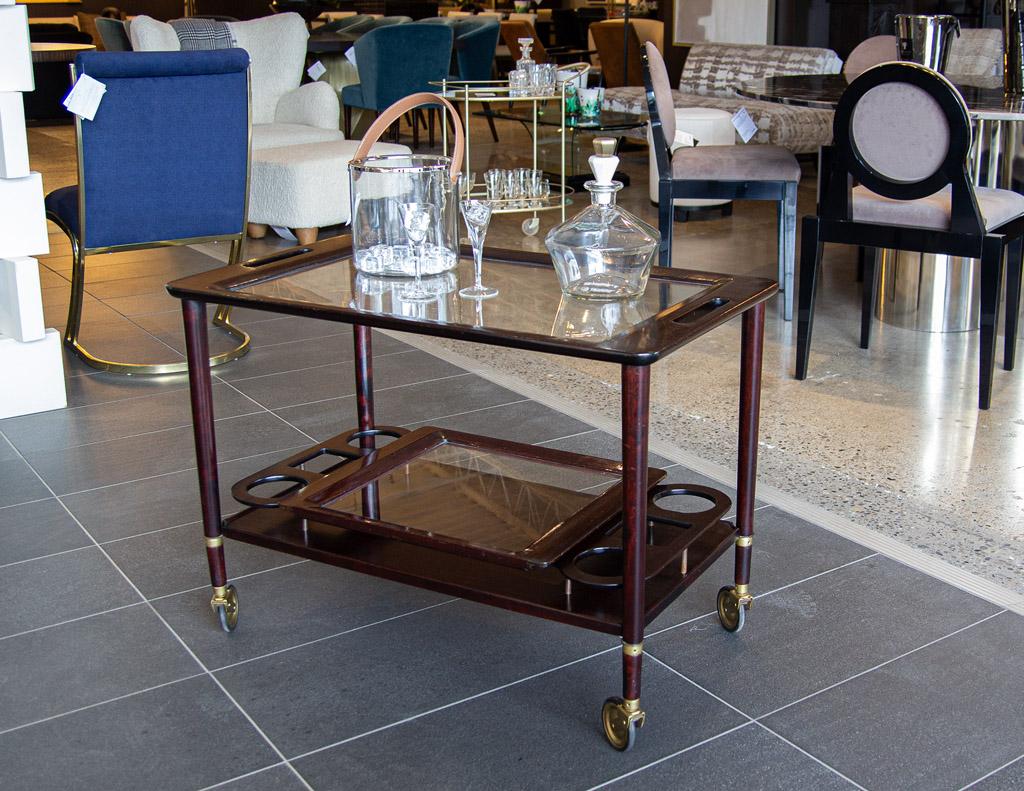 This stunning Italian bar cart is a perfect example of the elegant and timeless art deco style. Crafted from luxurious mahogany, this bar cart features beautiful brass accents and castors that add a touch of sophistication. Its removable serving