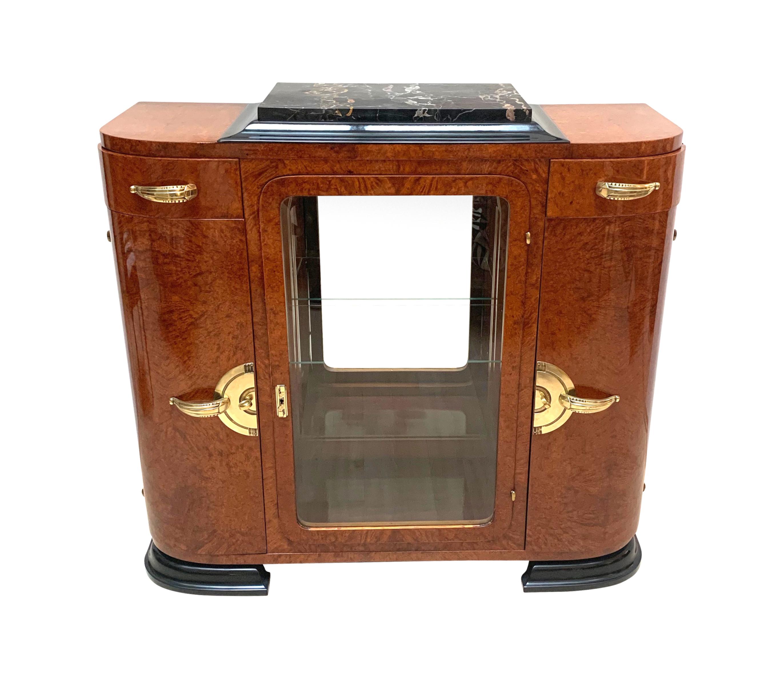 Gorgeous small Art Deco sideboard with open bar compartment in amazing Amboyna roots / burl veneer.
Three doors and two drawers. Two wooden doors with three shelf compartments inside. The middle vitrine door is made with a amboyna frame and a glass