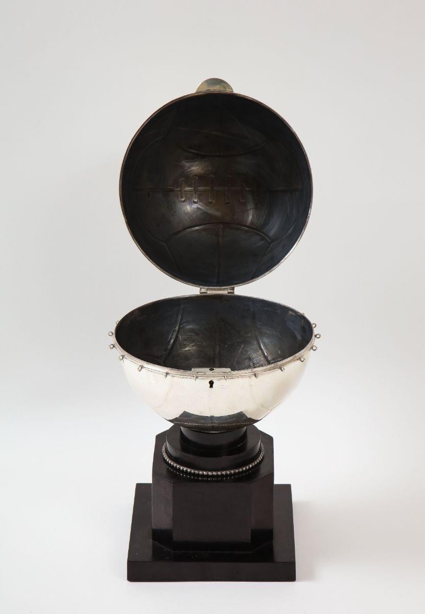 Una caja única Art Decó con tapa chapada en plata en forma de balón de baloncesto sobre un soporte lacado en negro con decoración de cuentas. Ideal para la entrada, las llaves, la cartera o para la oficina.