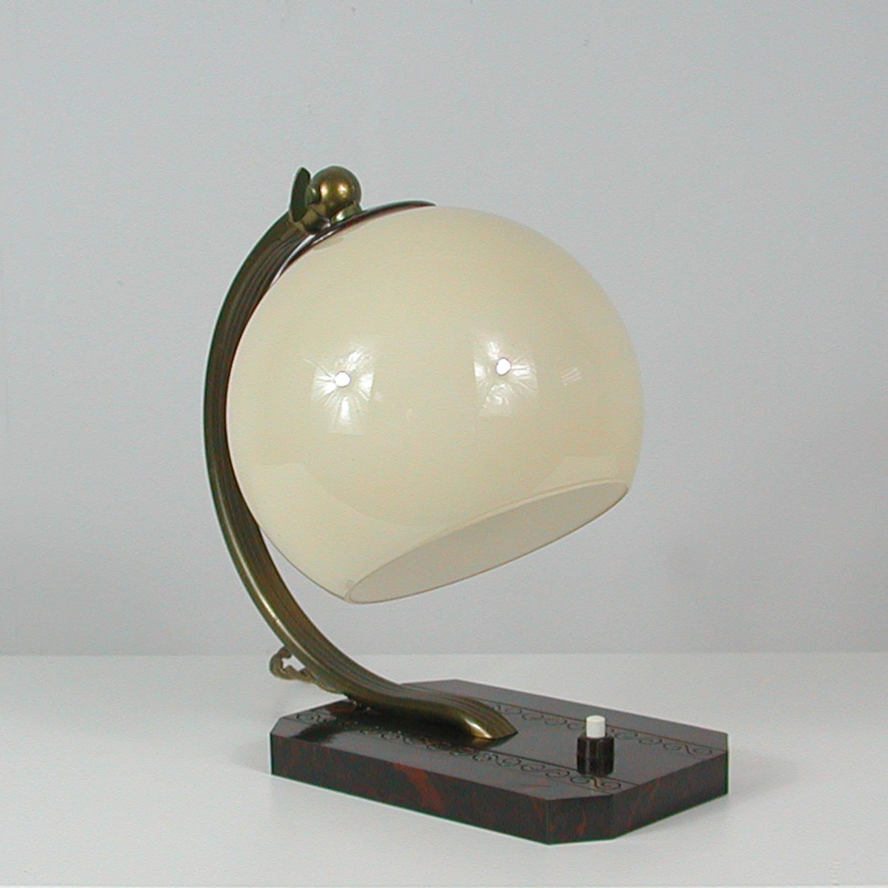 This unusual vintage table or bedside lamp was made in Germany in the 1930s-1940s during the Bauhaus period. It is made of bronzed brass, has got an adjustable lamp shade in ivory colored opaline glass and a brown marbled bakelite base. Original
