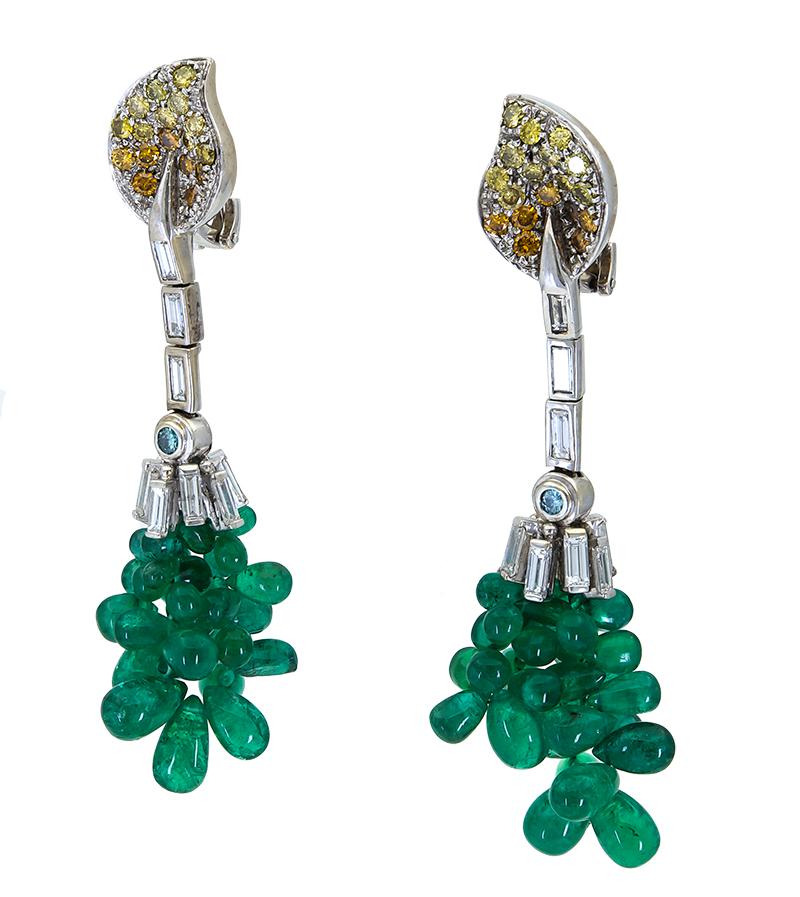 A unique and elegant style earrings made during the art deco era. Showcasing a cluster of oval-shaped beads made of lustrous green emeralds, suspended on a row of tapered baguette diamonds. Attached to a leaf design accented with orange and yellow