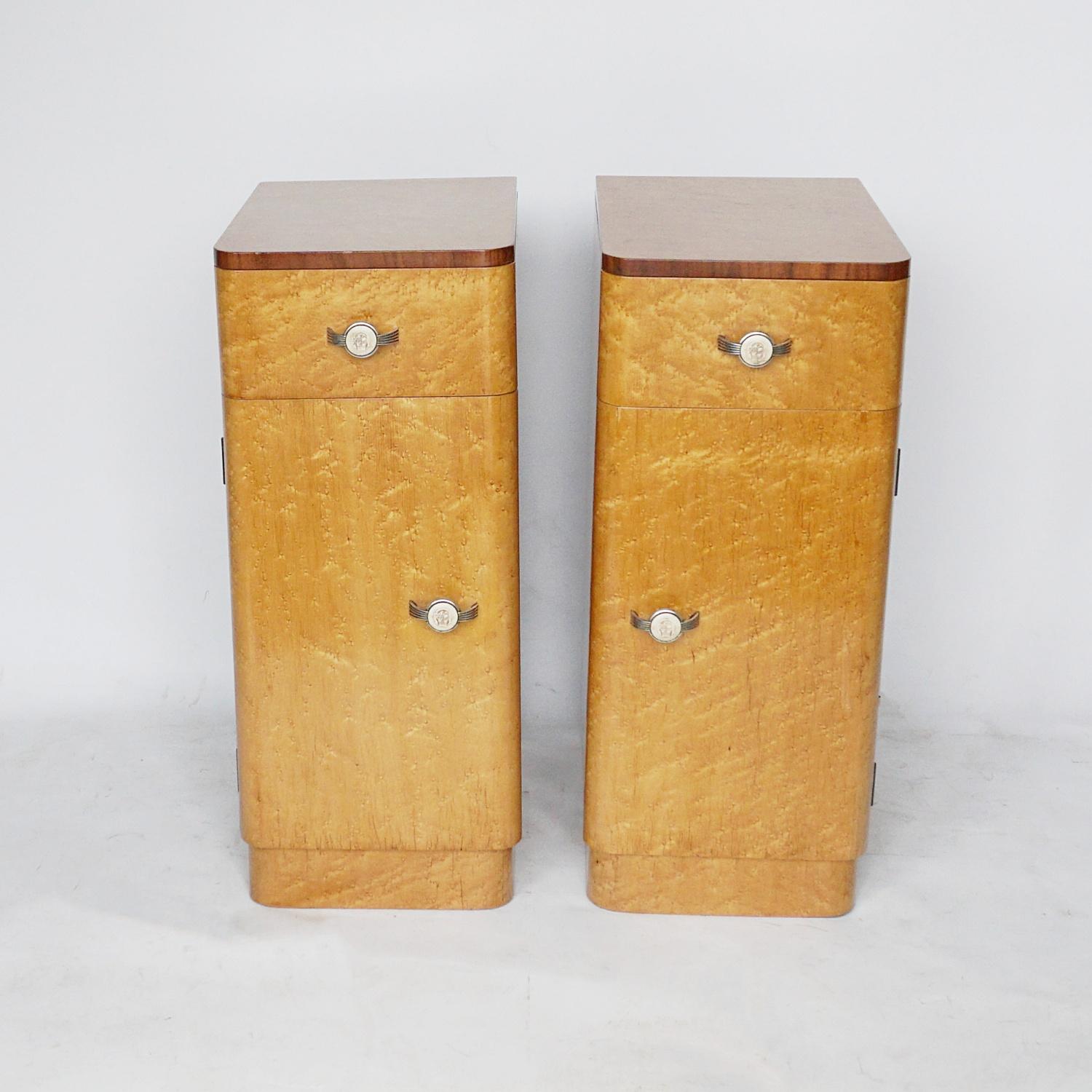 A pair of Art Deco bedside cabinets. Birdseye maple veneered with figured walnut banding. Original metal and carved bakelite handles. Upper drawer with lower shelved cupboard compartment. 

Dimensions: H 73.5cm W 37cm D 44cm

Origin: