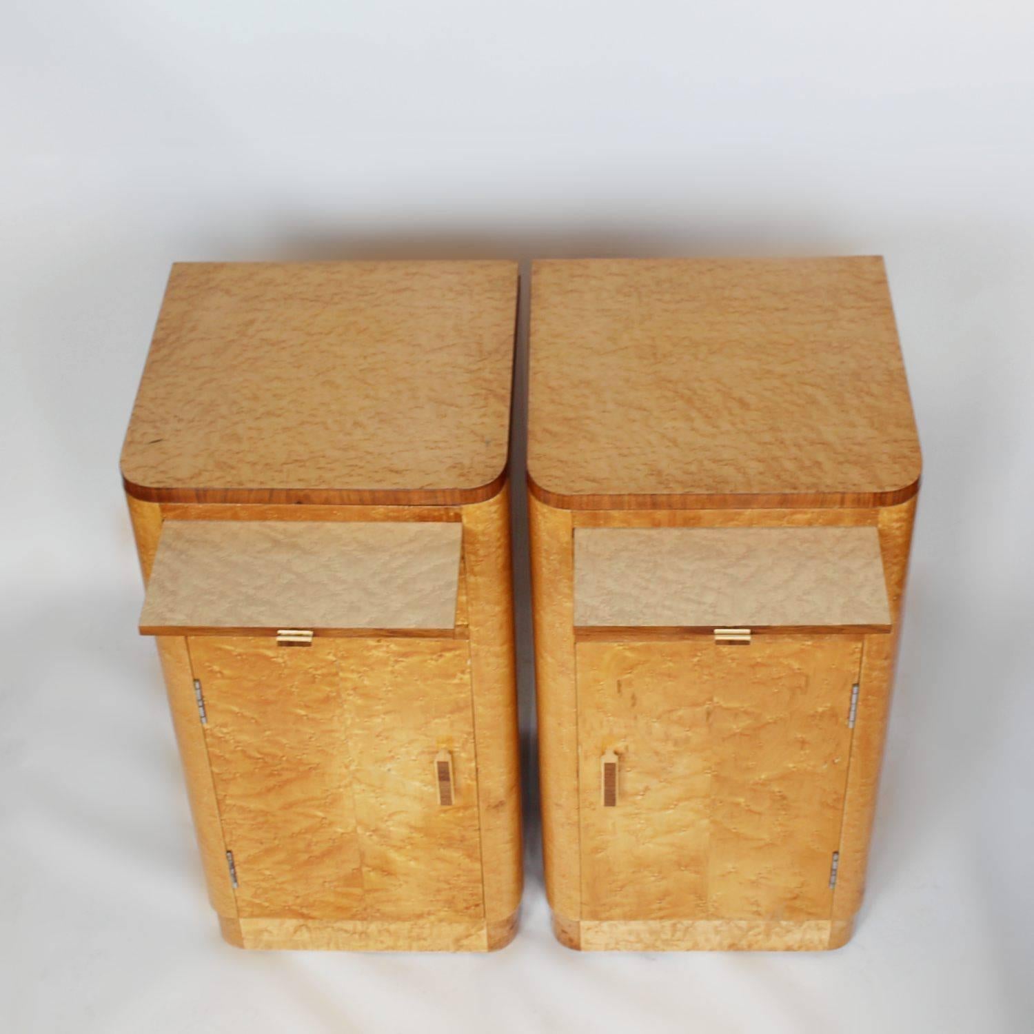 A pair of Art Deco bedside cabinets in Birdseye maple with walnut banding and original wooden handles. Integral sliding tray with single drawer and shelved cabinet below.
 
    