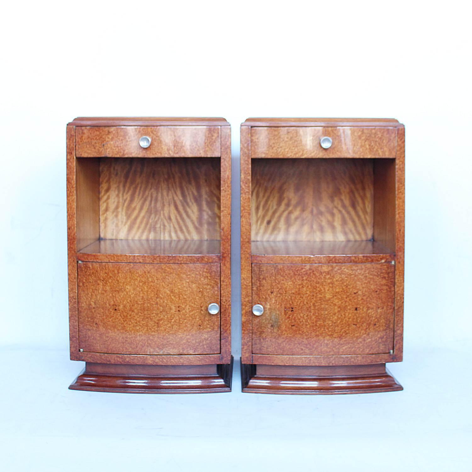 A pair of Art Deco, bedside cabinets. Amboyna veneers over solid mahogany, with stepped mahogany base and panelled back. Single drawer to top, satin birch backed shelf with cabinet beneath. Original metal handles.

 