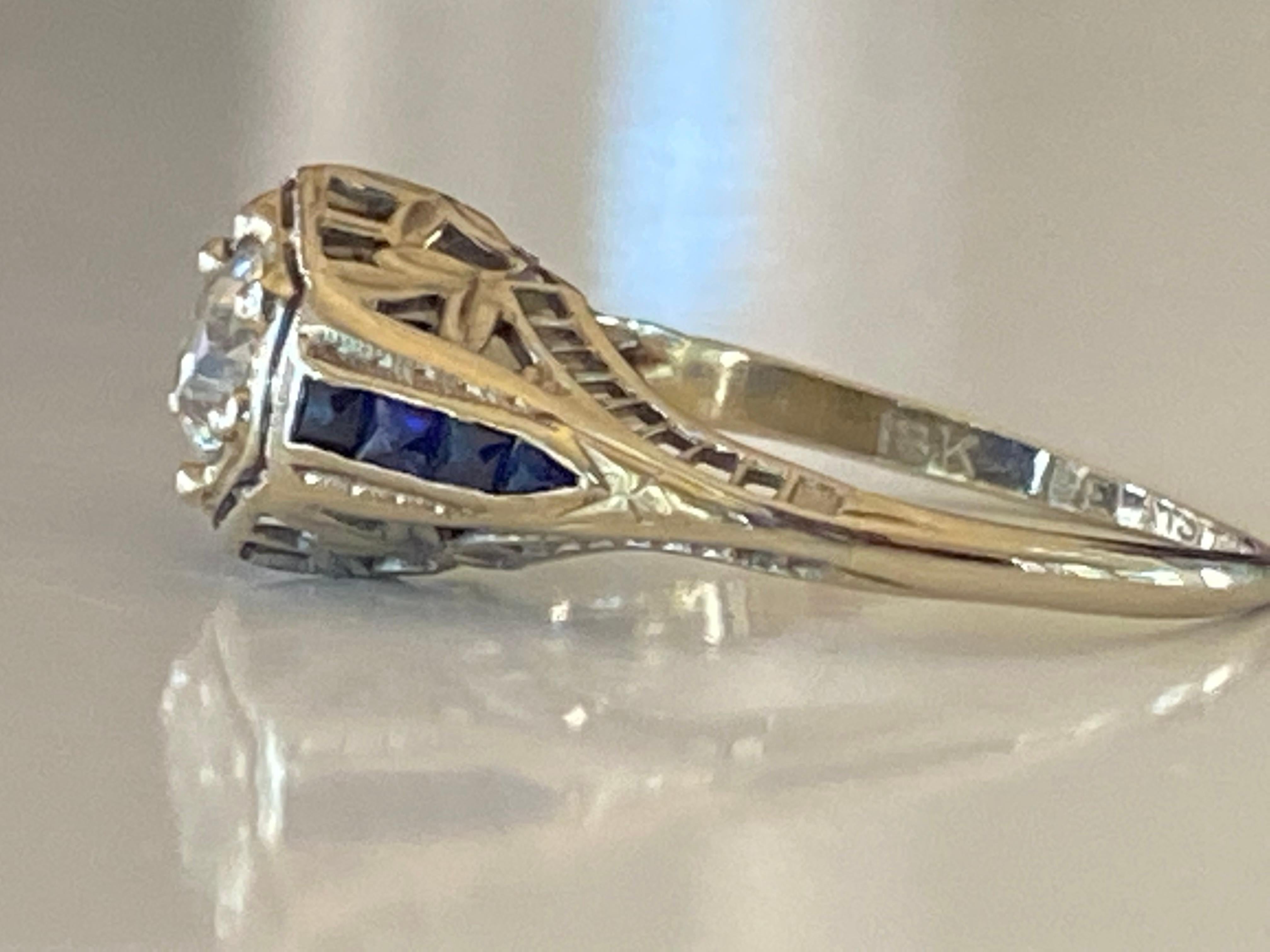 This striking Art Deco gem crafted in the 1920s in 18kt white gold features an Old European cut center stone totaling approximately 0.51 carats, I-J color, VS1 clarity complemented with two lines of sapphires and fine filigree details. Stamped 18K