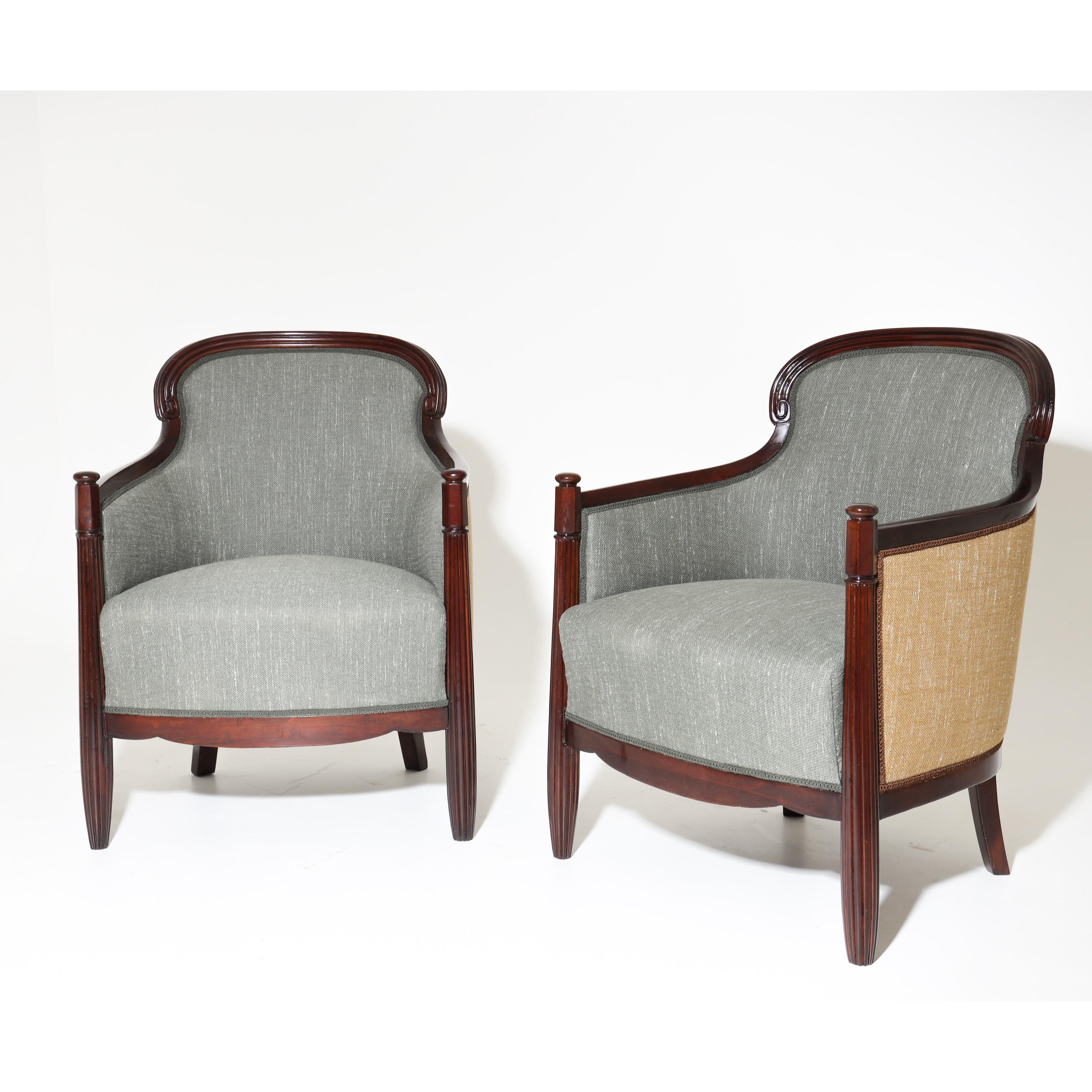 Pair of mahogany bergères on fluted conical front legs and slightly flared rear legs. The rounded backrest leads to the lower armrests, which end at the extended front legs. The armchairs are upholstered on all sides and were newly covered with a