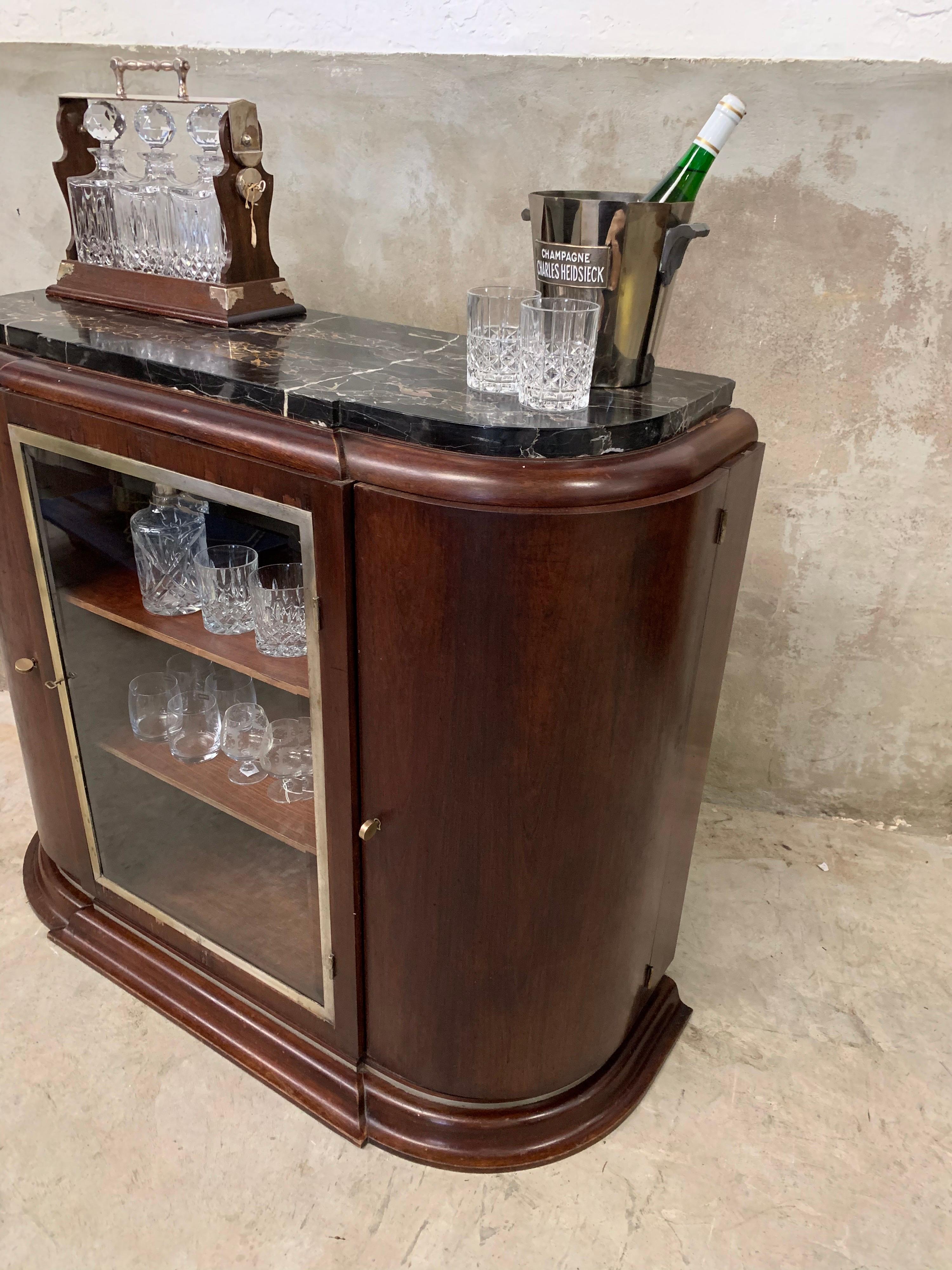 This Art Deco (beverage) cabinet is truly a rarity. Made in the 1920s-1930s and a real eye-catcher with its beautiful Portoro marble top, curved doors on the side and thick metal door with facet cut glass in the middle. Behind is a mirror. A part is