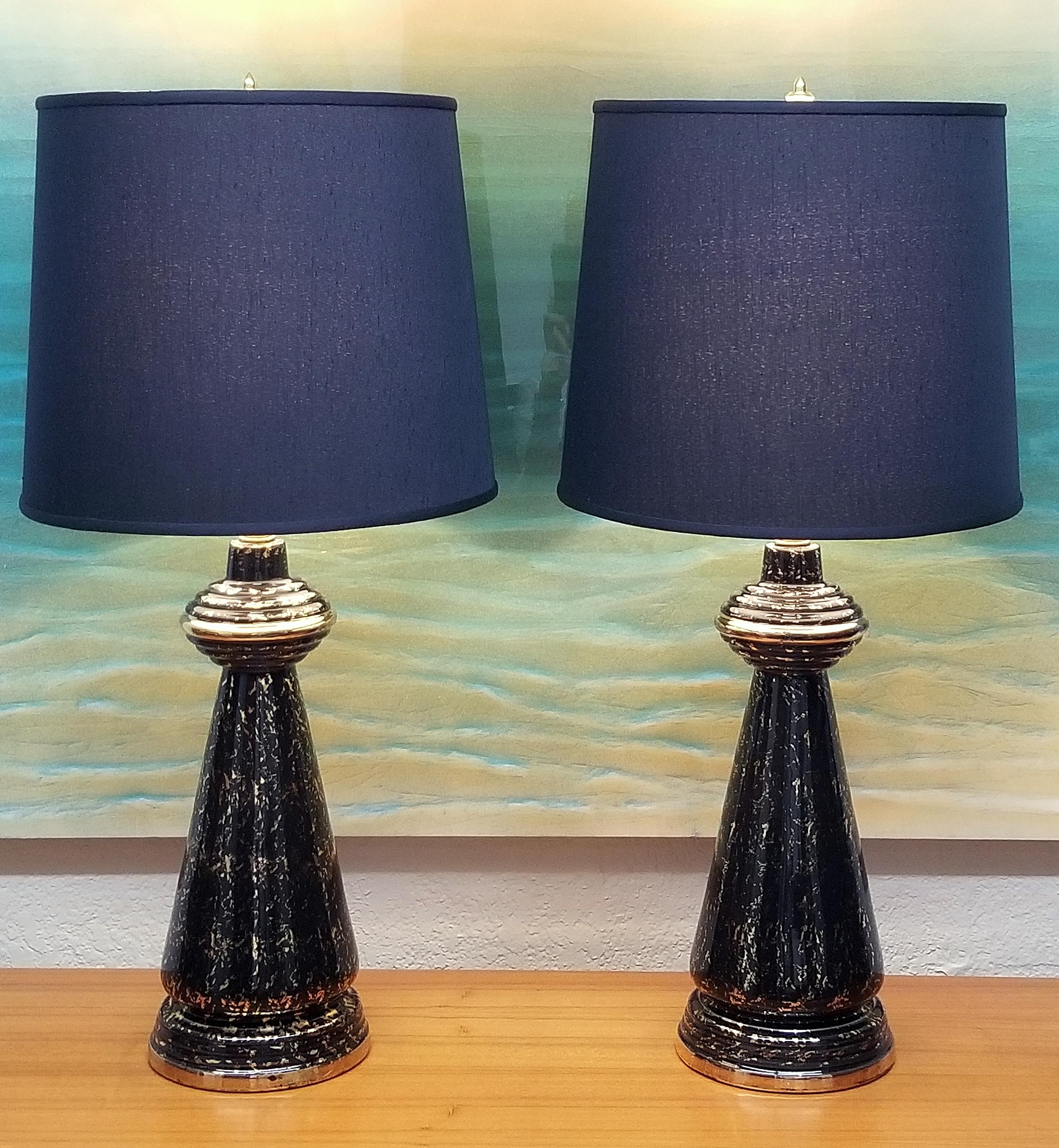 Pair of tall Art Deco black and gold porcelain lamps with new custom black silk shades. The impressive lamps have a fluted circular body in black and gold ceramic with reeded saucer shaped details. Very unique and decorative! Work well with many