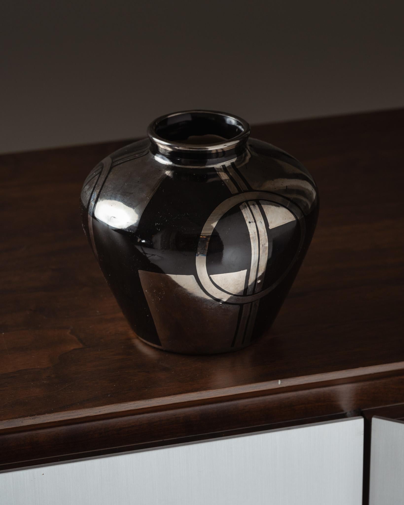Small Art Deco globe vase in ceramic, French manufacture, second quarter of the 20th century.
Black base highlighted with silver geometric decoration (circles and arcs), typical of the period. Wide, rounded body with a narrow neck. The