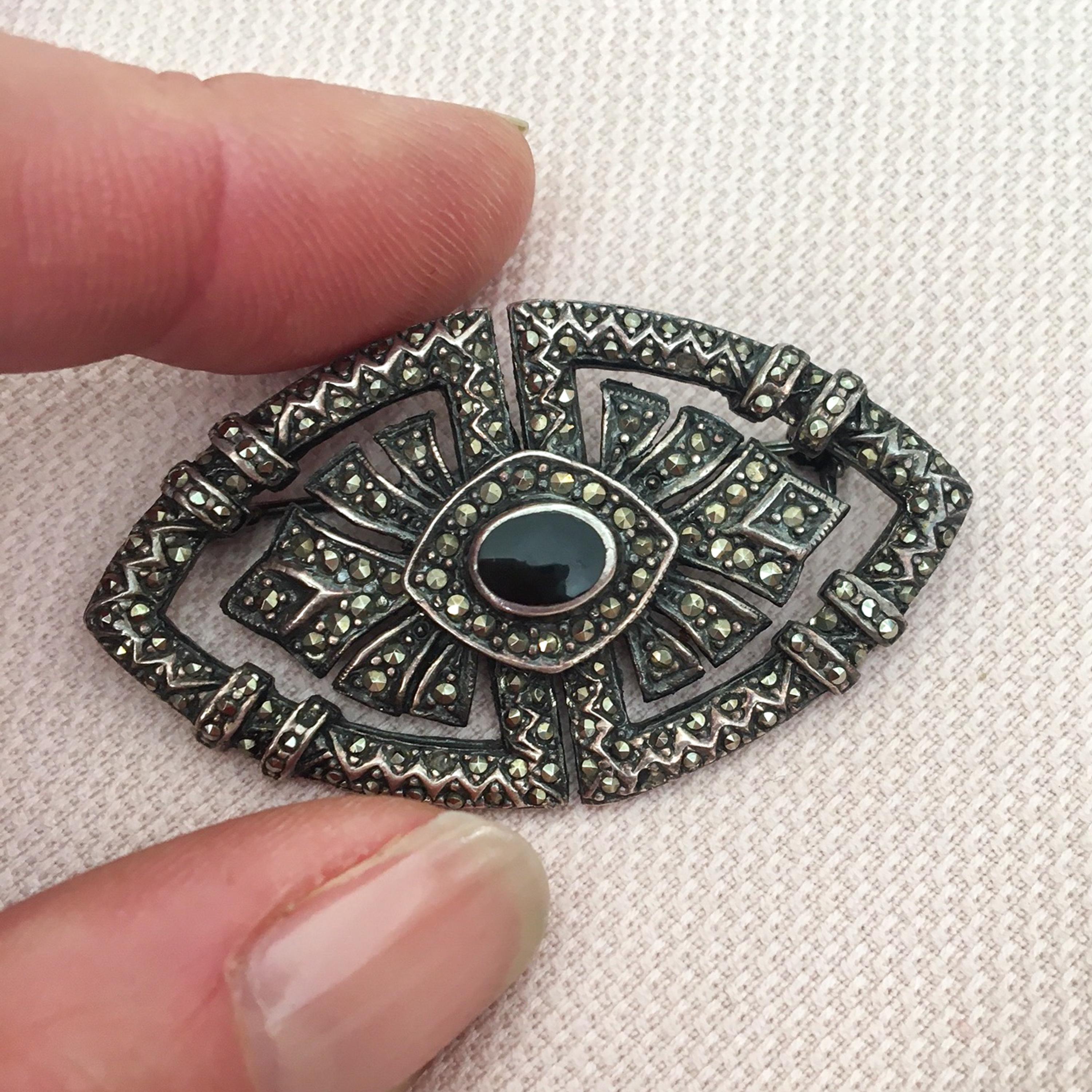 Art Deco silver brooch covered with marcasite stones and a center black onyx stone. This classic pin brooch has an openwork design and made of sterling silver set with many marcasite stones. The marcasite stones surrounds an oval black onyx stone at