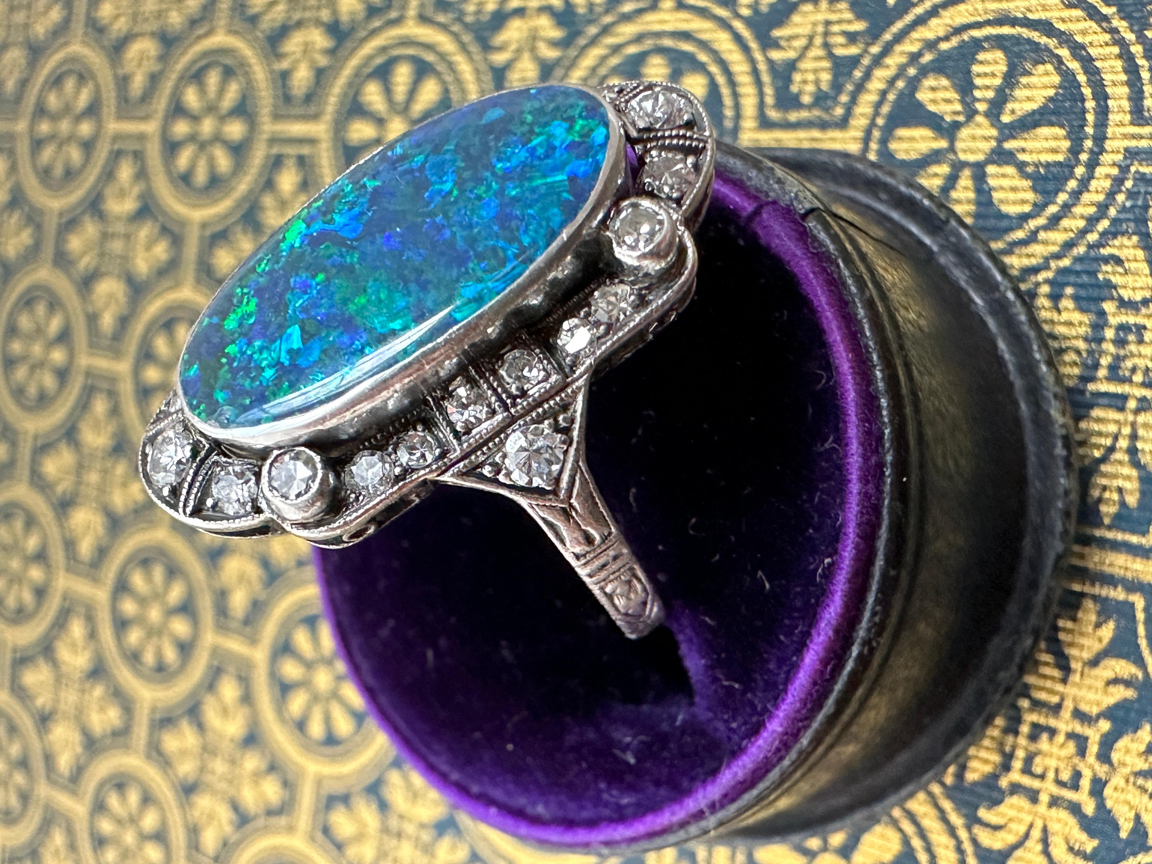 This magical Art Deco ring features a large black opal that shimmers with an ethereal play of colors, casting hues of bright cobalt blue, turquoise and neon green and yellow that shift as you move your hand. Hand crafted in platinum, the opal is