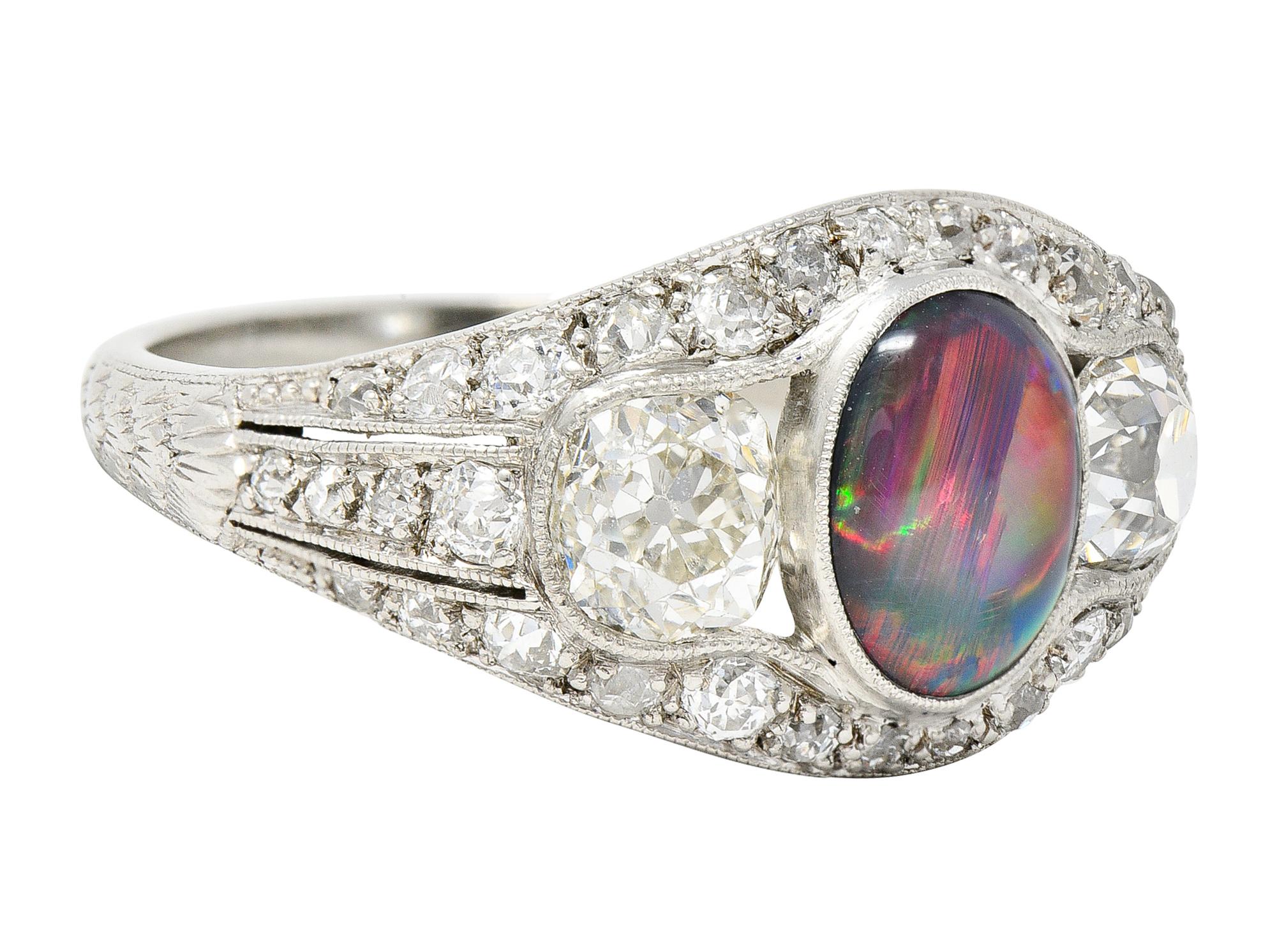Centering an oval shaped opal cabochon measuring 8.5 x 6.5 mm - bezel set. Opaque black in body color with strong spectral play-of-color. Flanked by two old mine cut diamonds weighing approximately 1.30 carats total. H/I color with VS clarity -