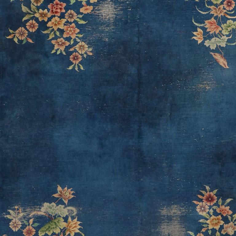 An Art Deco Chinese Chinoiserie rectangular rug in blue with bouquets of pink, yellow, purple, and green flowers at each corner. 

On a deep blue or navy background, each corner of this floor covering is festooned with yellow, pink, and purple