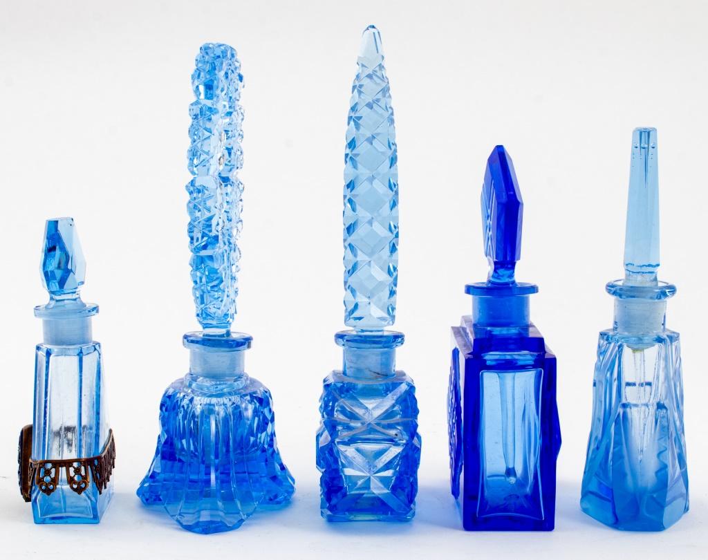 Group of five cut glass perfume bottles, likely Czech, comprising one Art Deco cobalt blue bottle with colorless glass dropper, and four ice blue perfume bottles, one with frosted glass details, and one with floral metal mounts.

Dimensions: