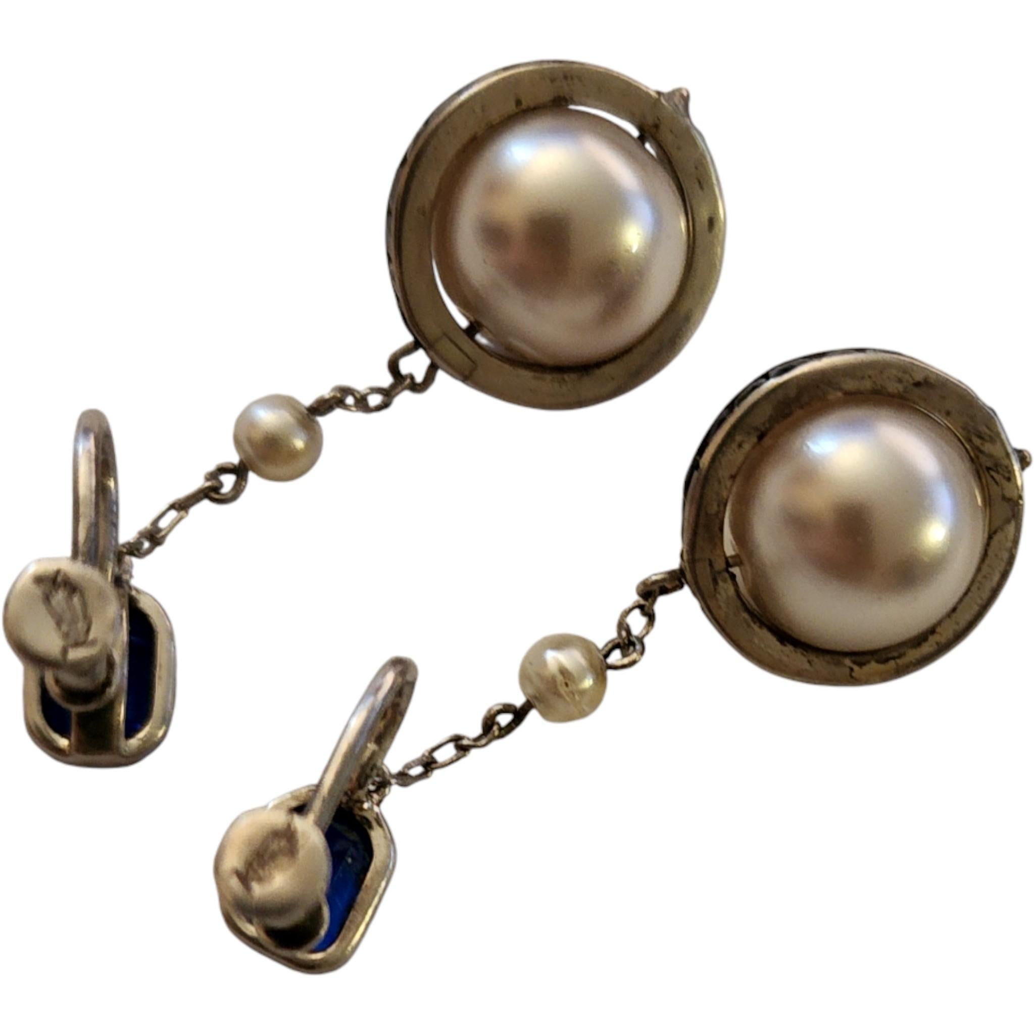 These vintage Art Deco-style dangle earrings feature a dramatic combination of bold cobalt blue glass, luminous faux pearls, and sterling silver .925 setting. The earrings begin with an octagonal faceted blue glass stud, followed by a delicate