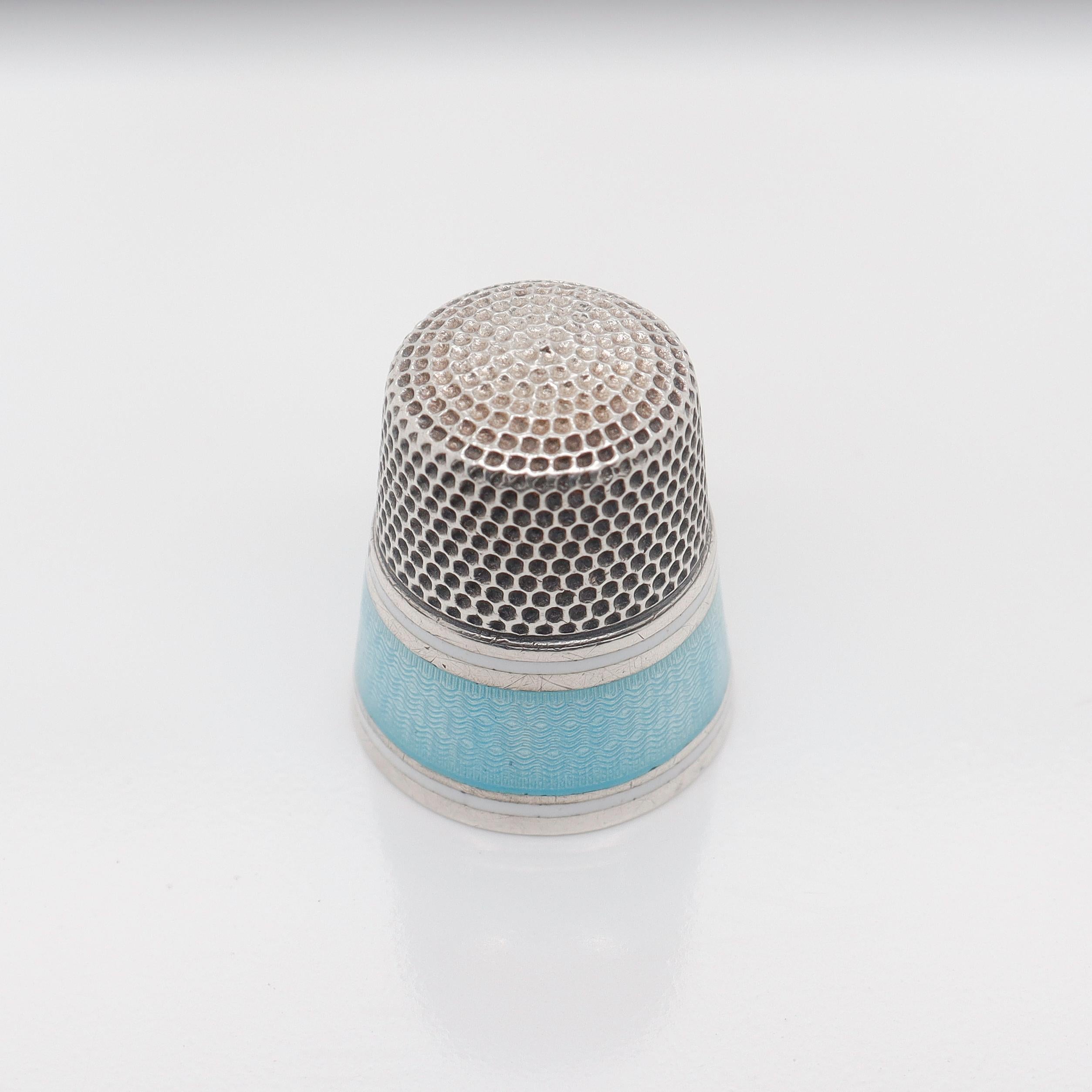 A fine antique American thimble.

By Simmons Brothers.

In sterling silver with a band of guilloche enamel flanked by two thin bands of white enamel around the circumference.

Marked to the interior with the number 11 (likely a size) as well as with