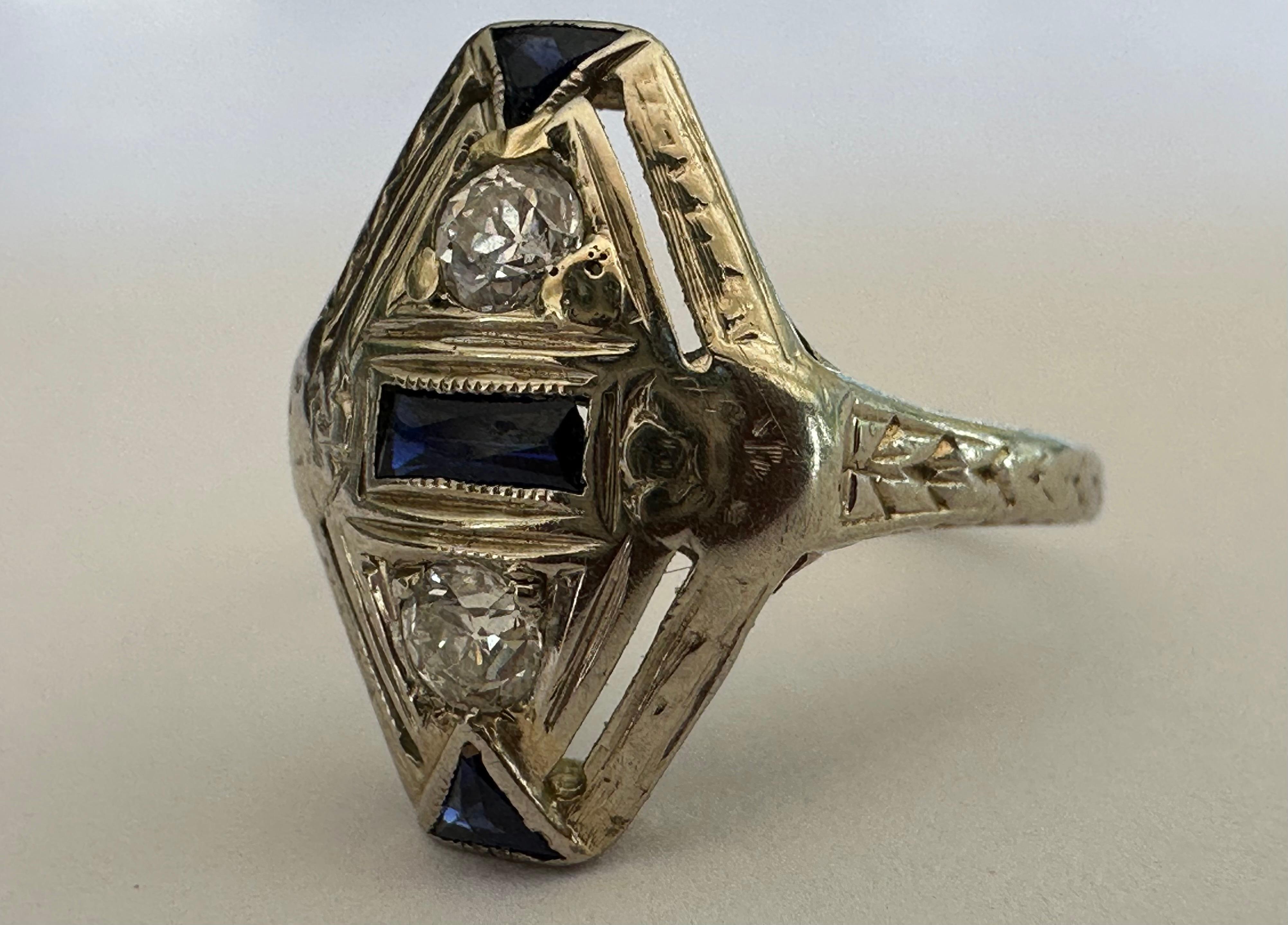 Two Old European cut diamonds totaling approximately 0.16 carat, HI color, VS clarity, shine within this navette-shaped pinky ring, complemented with deep blue sapphire accents and decorative piercing and hand engraving throughout.   Set in 18k