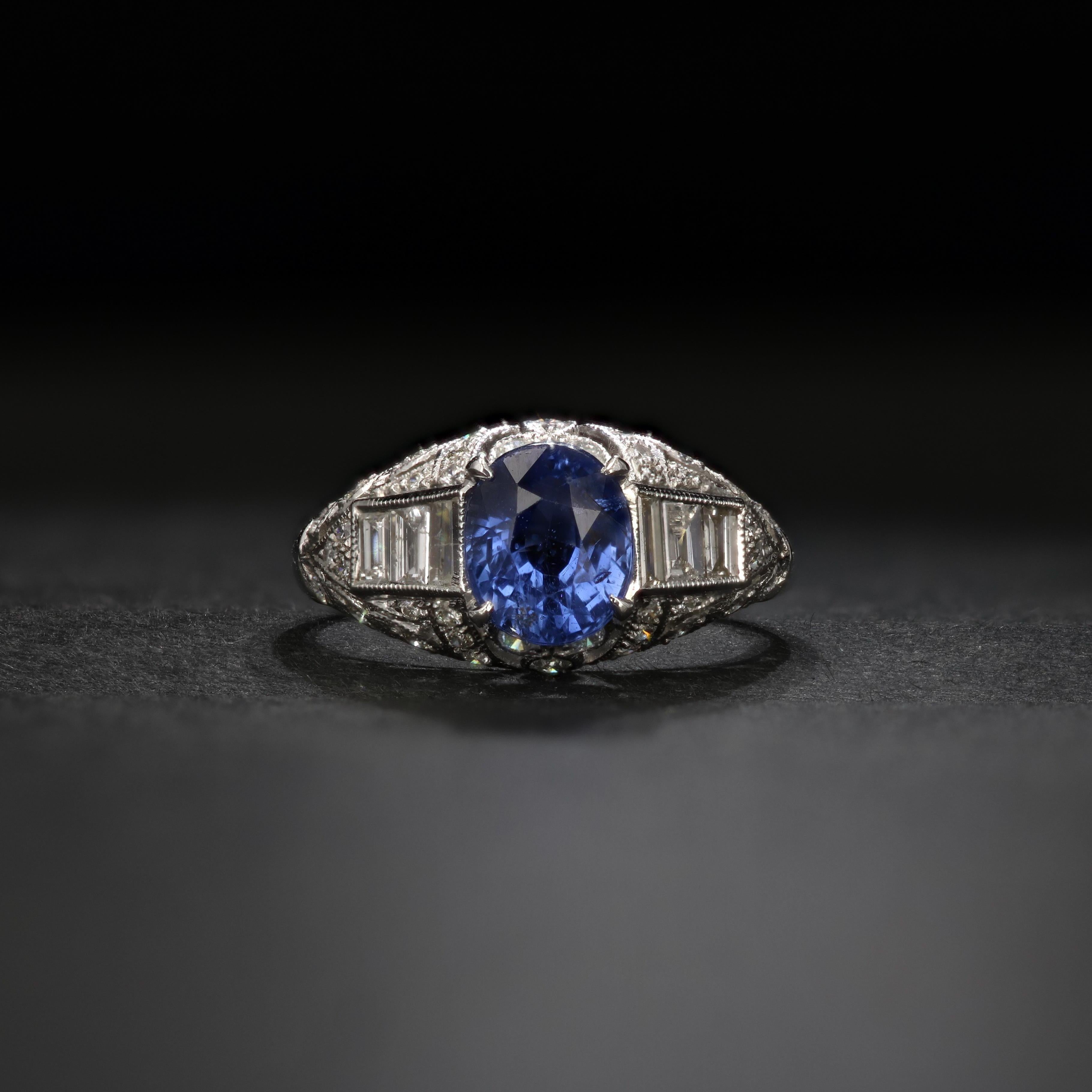 An exquisite Art Deco Style sapphire and diamond ring set in 18k white gold. This ring features an oval sapphire of approximately 2.04 carats. The sapphire is a vivid cornflower blue with excellent clarity. Surrounding the sapphire are approximately