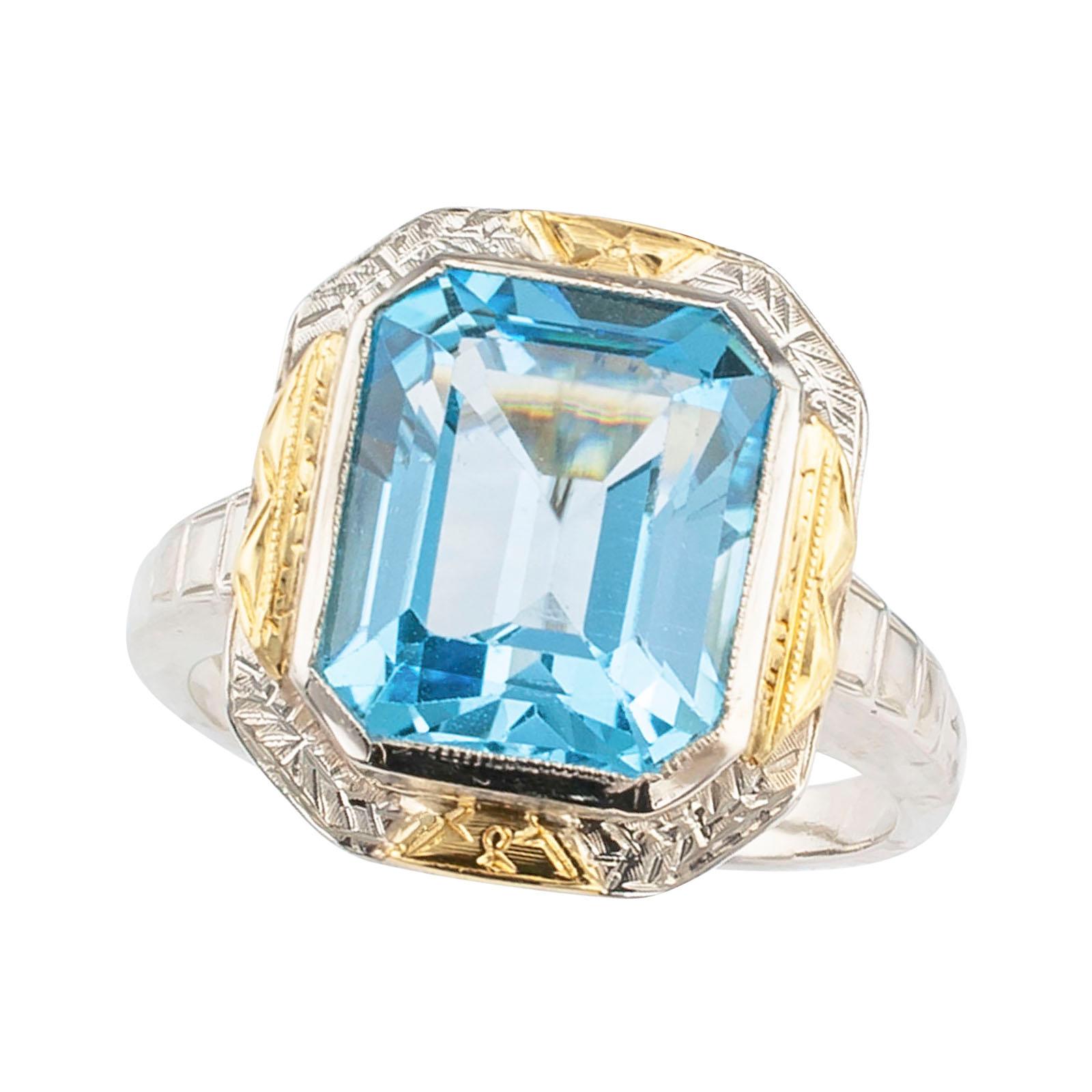 Art Deco blue topaz and two-tone gold ring circa 1930.

DETAILS:
GEMSTONE: one emerald-cut blue topaz.

METAL: white and yellow 14-karat gold.

RING SIZE: approximately 5 ¾, can be resized.

MEASUREMENTS: approximately 9/16” (14 mm) wide across the