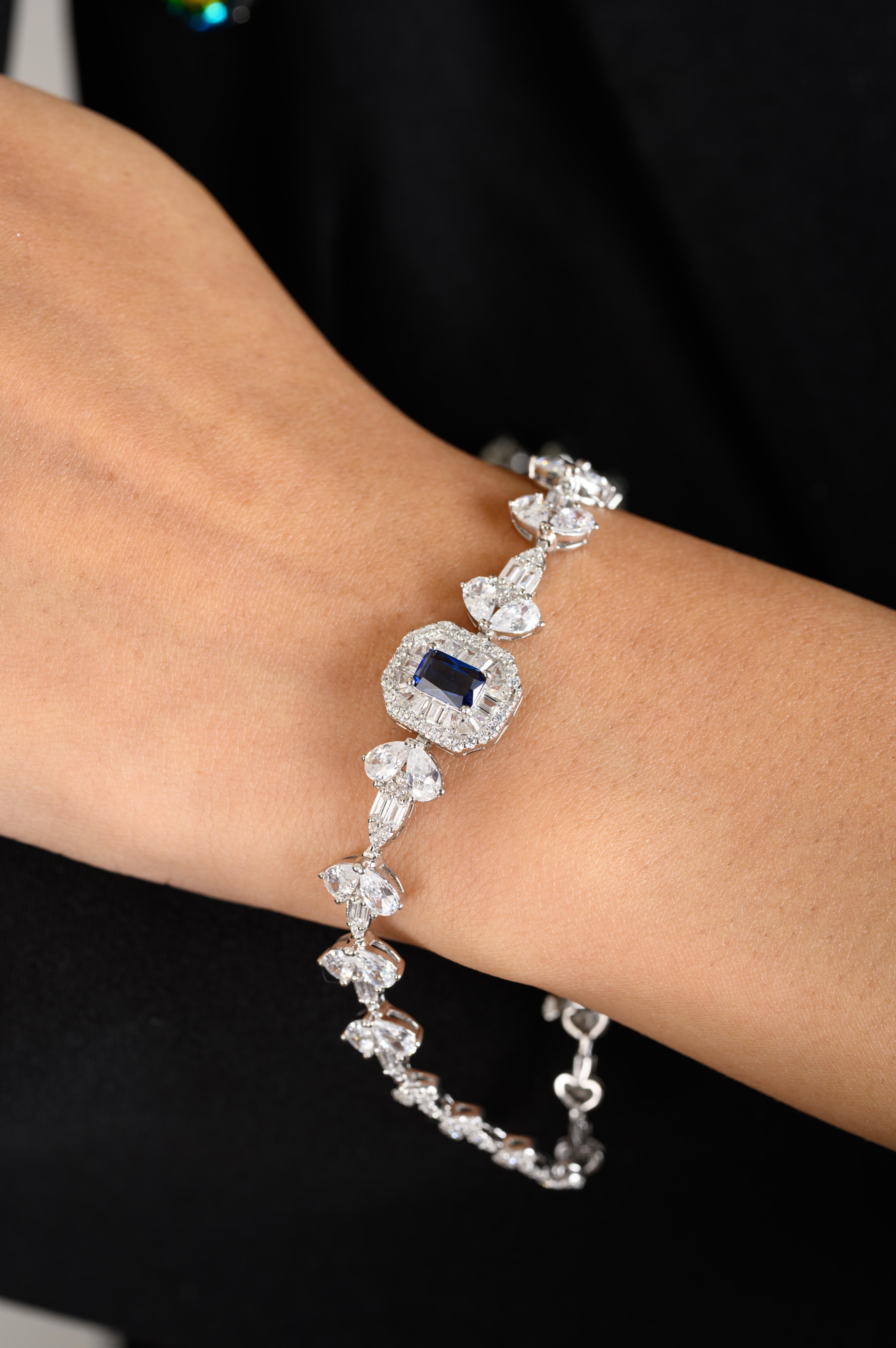 Graceful and luminous, this 925 sterling silver bracelet showcases a striking emerald-cut blue zircon at its center, encased in a double halo of shimmering rhinestones. The band features an exquisite array of pear-shaped rhinestones, arranged in a