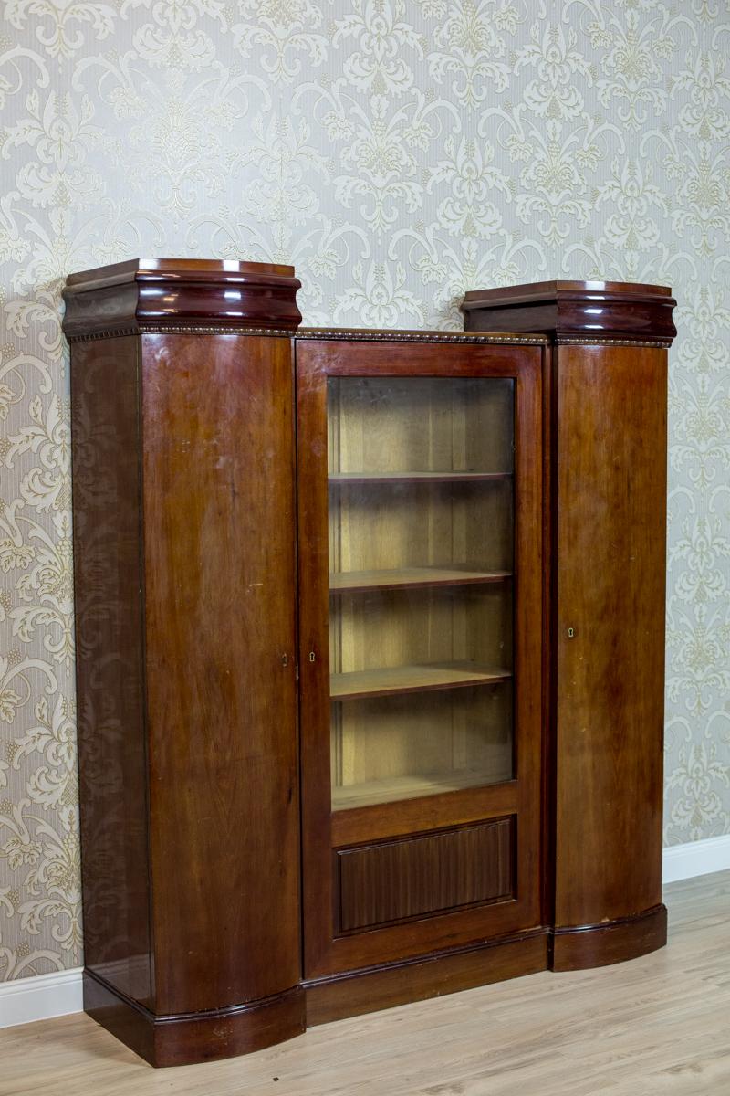 We present you this three-door piece of furniture. The central section is lower, glazed on the three quarters of its height.
The corner segments with full doors with semi-circular fronts.
The top of this bookcase is finished with a molding with